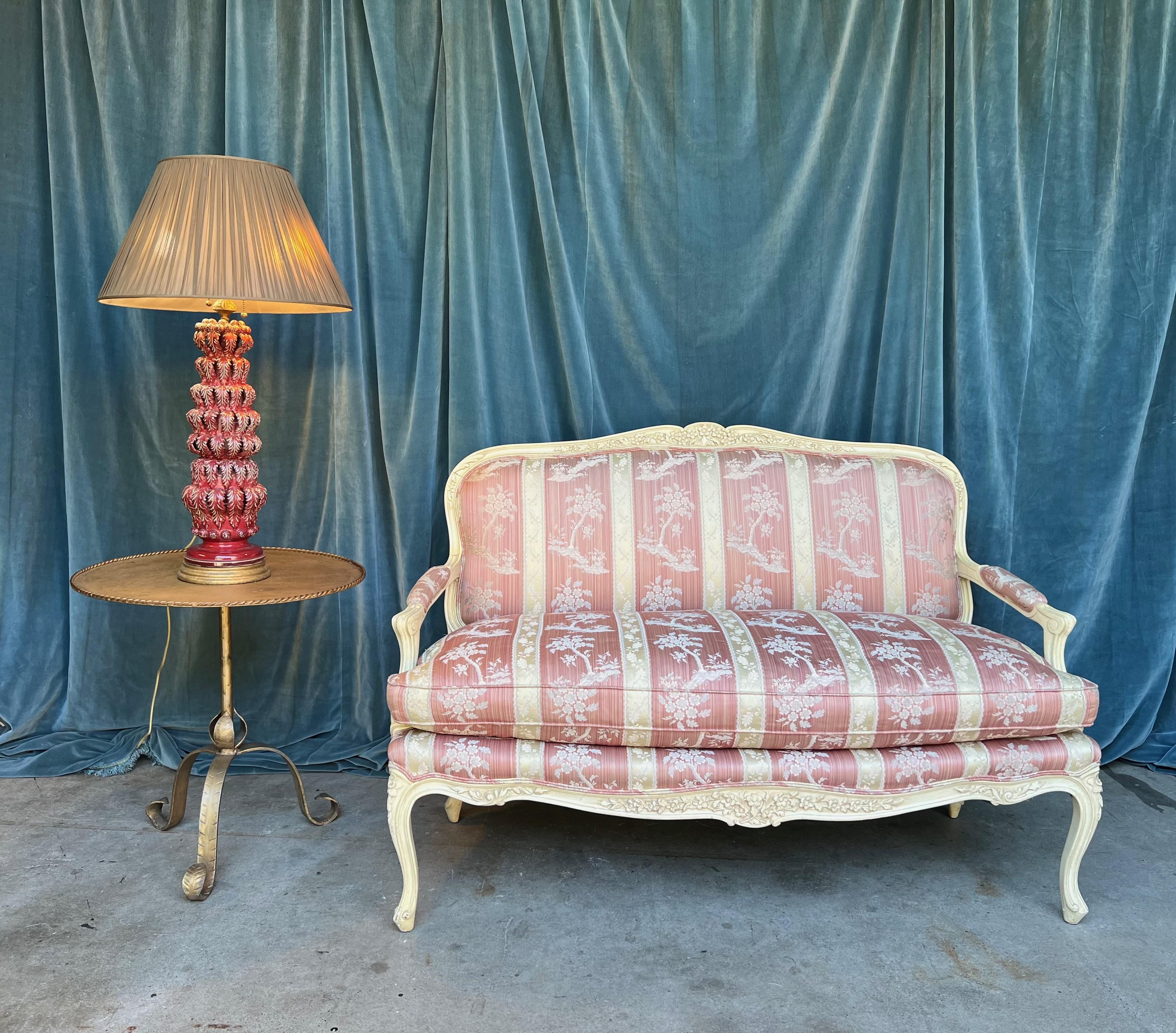 This elegant French 20th century settee in the  Louis XV style, had a painted wooden frame in a delicate cream shade, harmonizing perfectly with the upholstery, a blend of pink florals and cream stripes.  This settee is in good vintage condition and