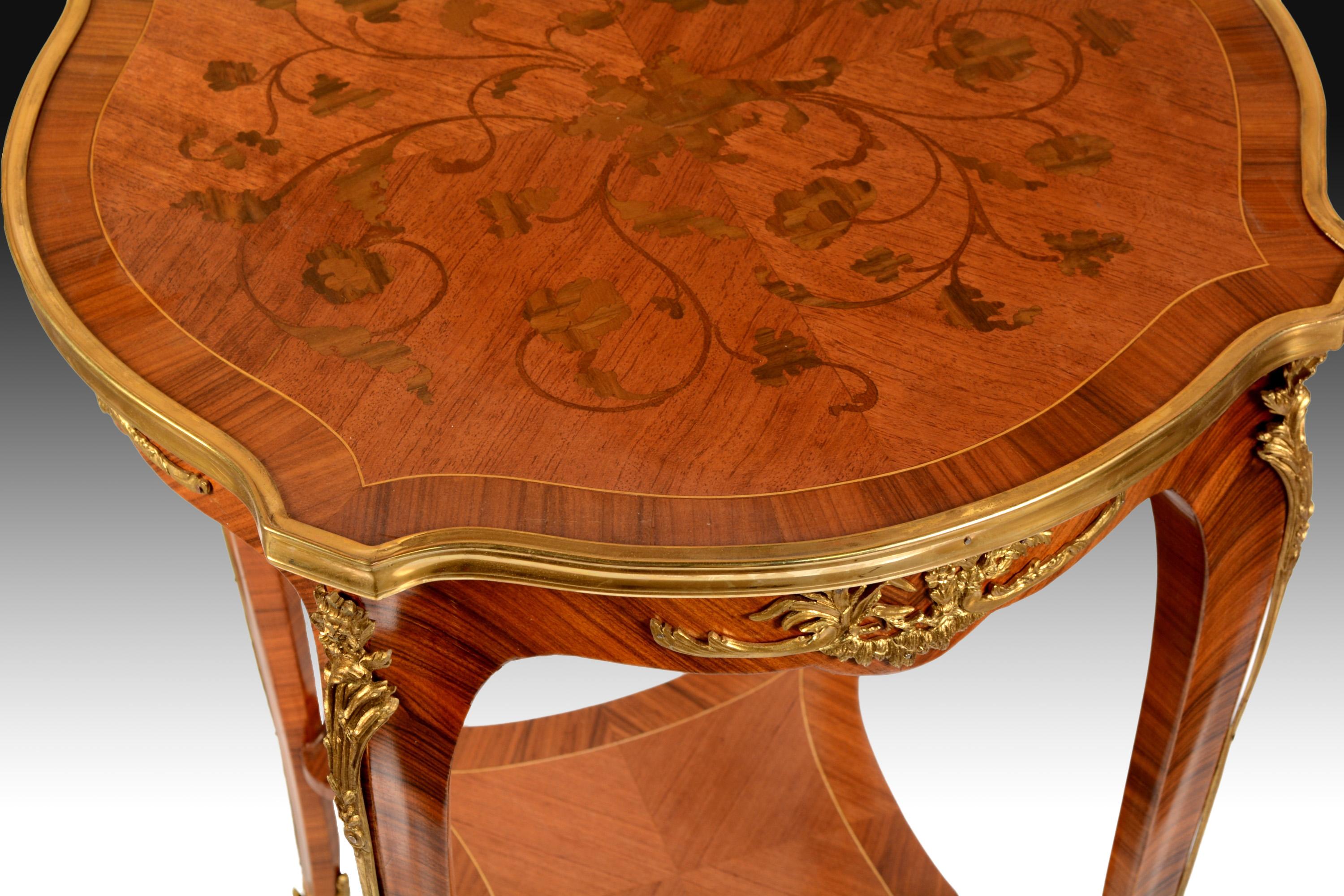 The four cabriolet legs have been joined in their inferior part with a square shelf of concave edges and they have been decorated with vegetal elements in golden bronze, like the waist of the table. The top panel, round with straight extensions,