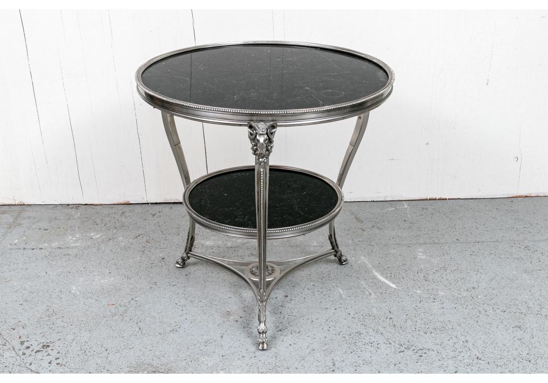 Table d'appoint ronde en bronze argenté de style Louis XV avec garniture cannelée et insertion de marbre noir belge sur bois. La table avec des motifs de tête de bélier est jointe à un niveau inférieur conforme et à un châssis triangulaire bien