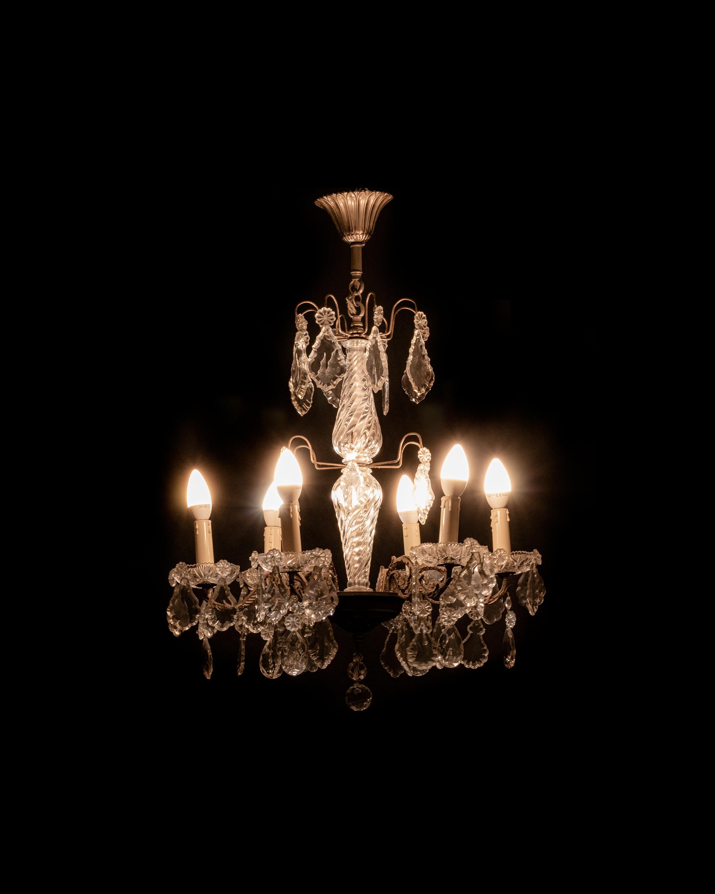Araña de estilo Luis XV de seis luces, con brazos de bronce ornamentados, colgantes de cristal y una columna central de cristal tintado. 
Esta lámpara de araña francesa del siglo XX combina las curvas clásicas del Rococo con un radiante trabajo en