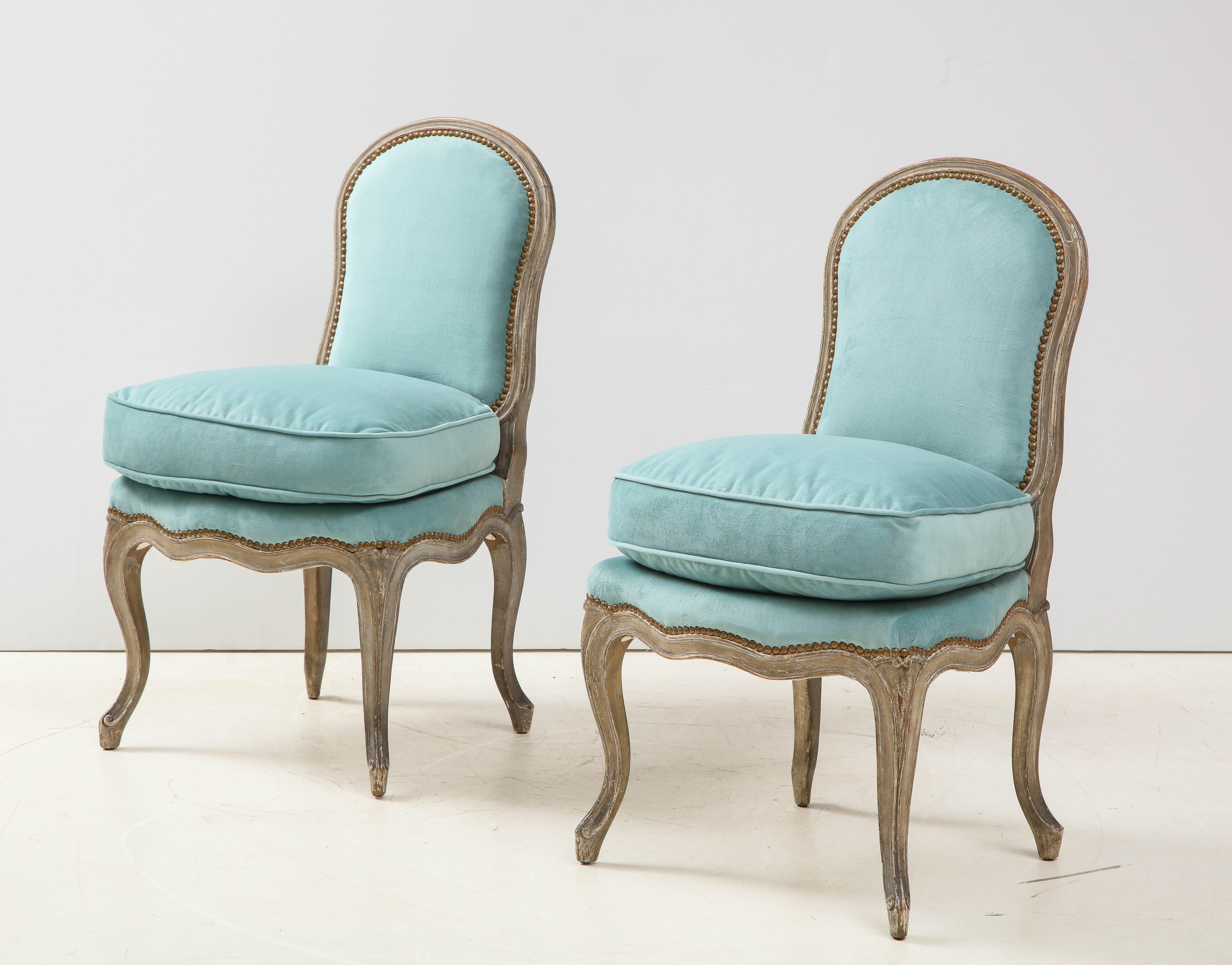 A charming pair of Louis XV style slipper chairs with a painted finish, a tight back and loose seat cushion, trimmed in nail heads. Upholstered in a lovely blue, this duo would be perfect as extra seating in living room or accent chairs in a bedroom