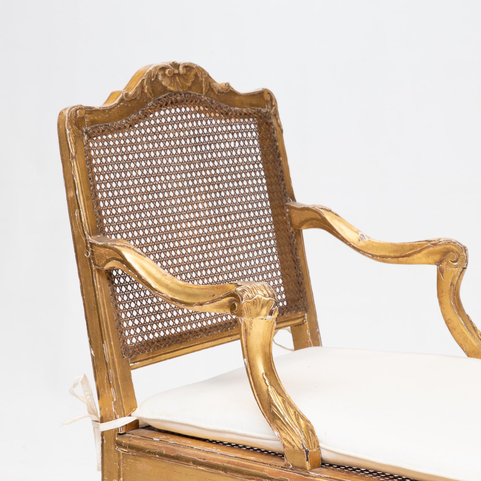 A Louis XV style gold chaise lounge with cushion seat over the cane. The cane is in good condition to the back and seat. Nicely worn gold finish with gesso showing through. Very unique size. Ready for use.