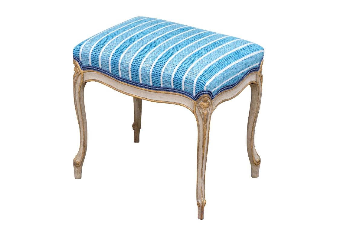 An upholstered bench with a light-colored frame having subtle gilt (gold) accents characteristic of Louis XV furniture to enhance the ornate carvings. The overall design emphasizes flowing, serpentine lines and a lighter appearance. The carved apron