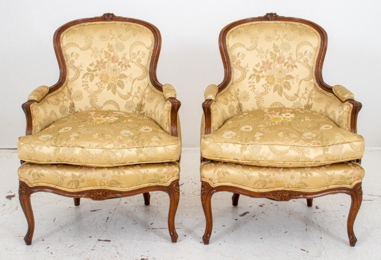 French Louis XV style pair of bergeres or armchairs, carved fruitwood with floral patterns on back, and a shaped seat with cushion, upholstered in a beige damask silky fabric, above cabriole legs with scroll feet.

Dimensions: 37