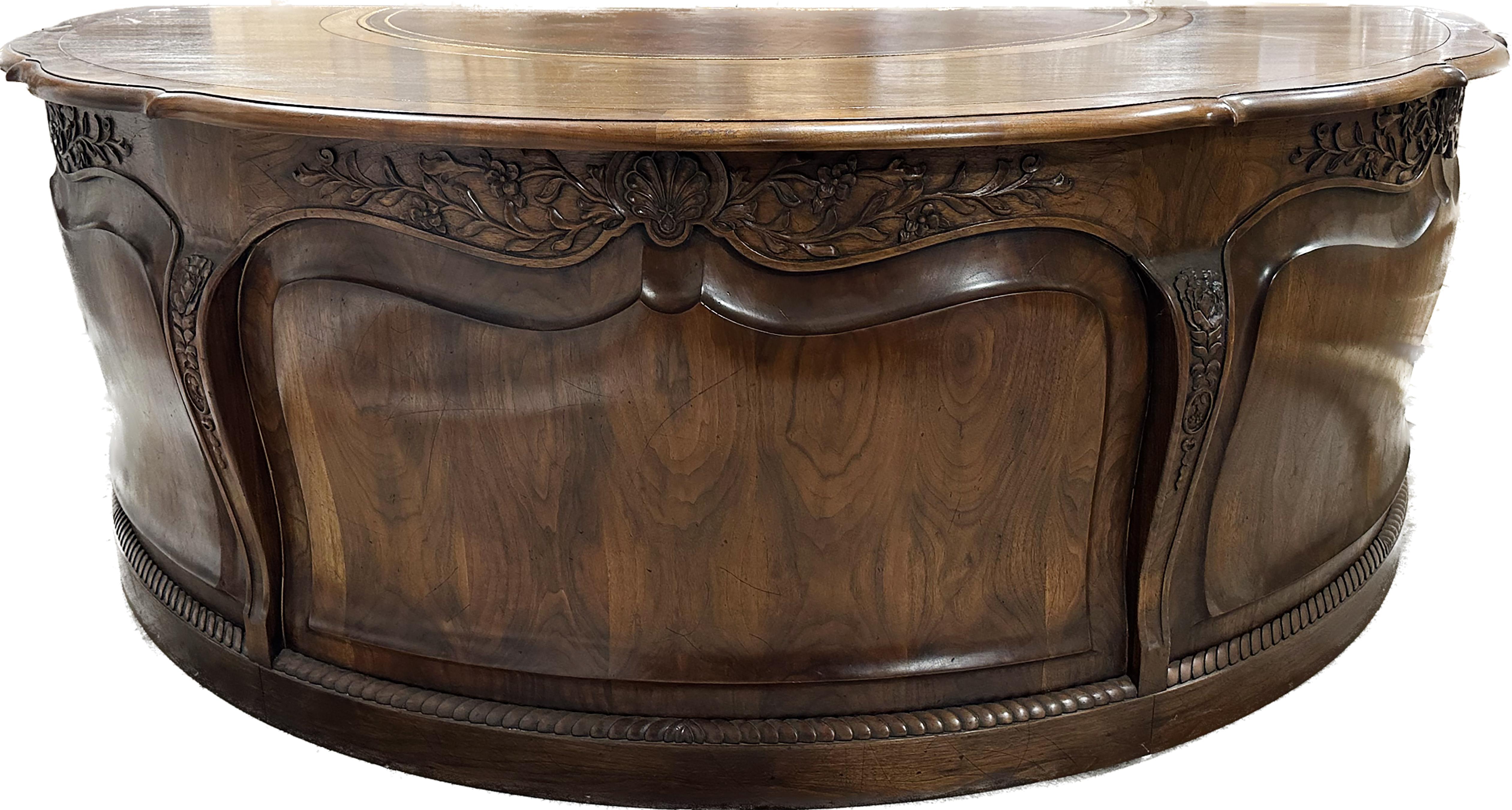 A monumental Louis XV style walnut carved serpentine demilune executive desk.  Ornate carvings on the outside including carved floral shapes over a scalloped front and a rope pattern at the bottom. Leather embossed top with gilt trim. Two cabinets
