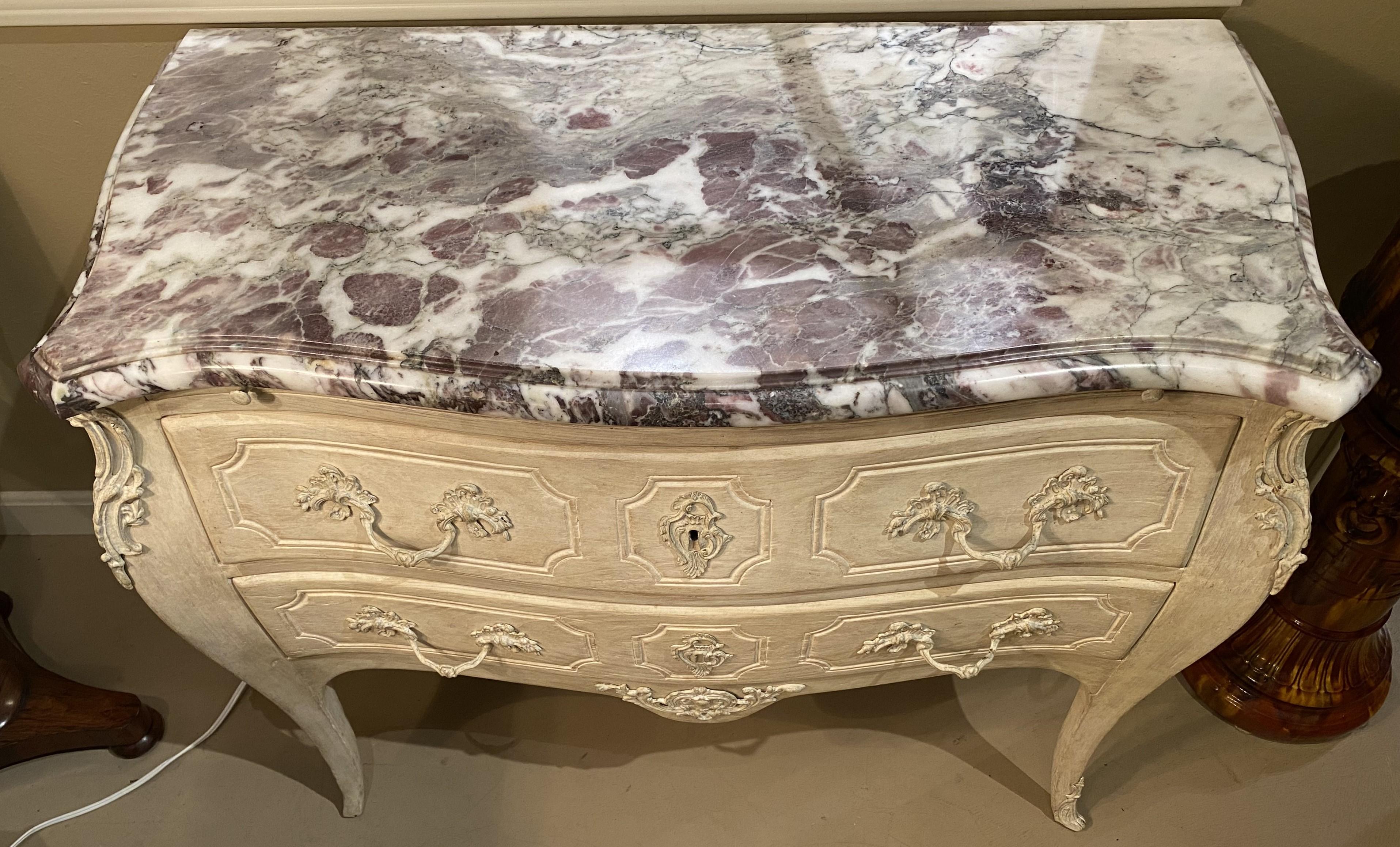 A fine Louis XV style French white washed two drawer commode in a serpentine form with conforming molded Levanto style marble top, foliate carved corner decoration, applied drawer front handle accents, and center drop, all supported by cabriole