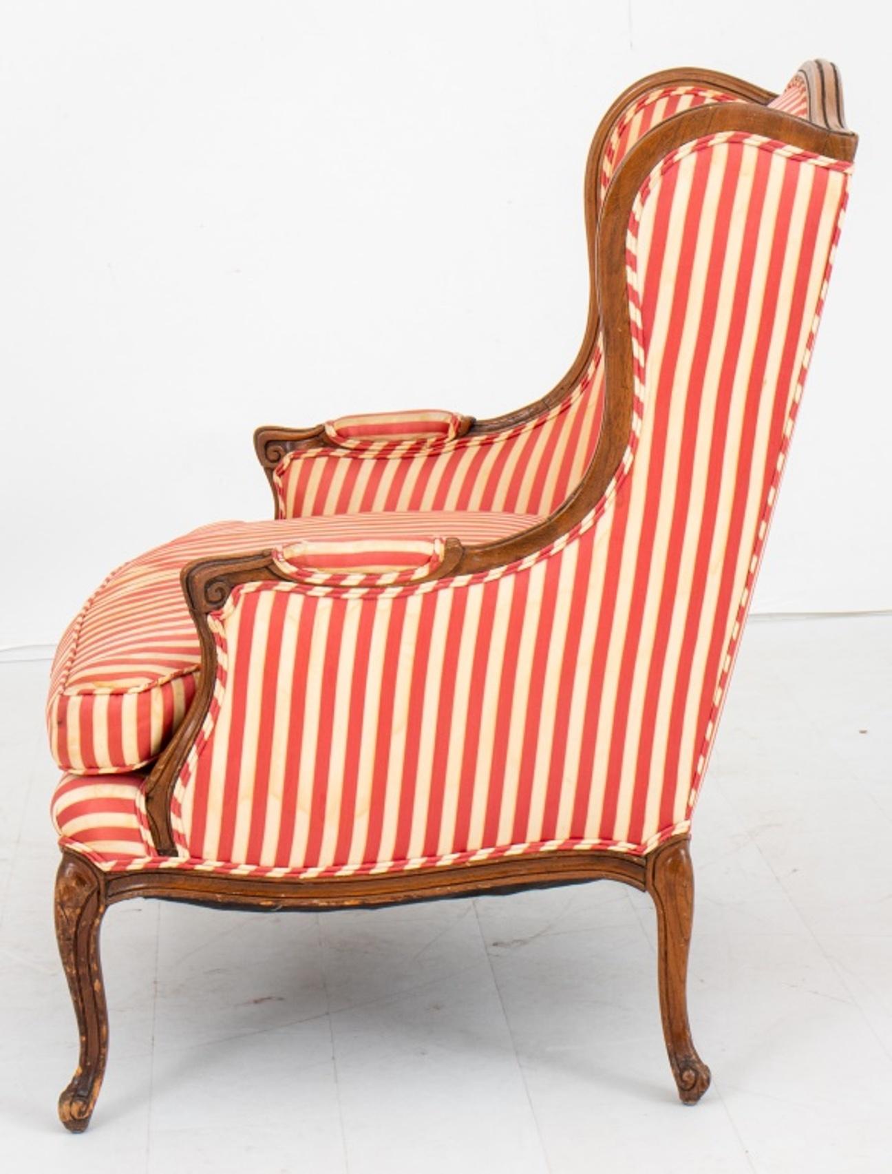 Louis XV style wing chair or bergere, overall upholstered in a red and white awning stripe, the molded frame above four cabriole legs.

Dimensions: 38