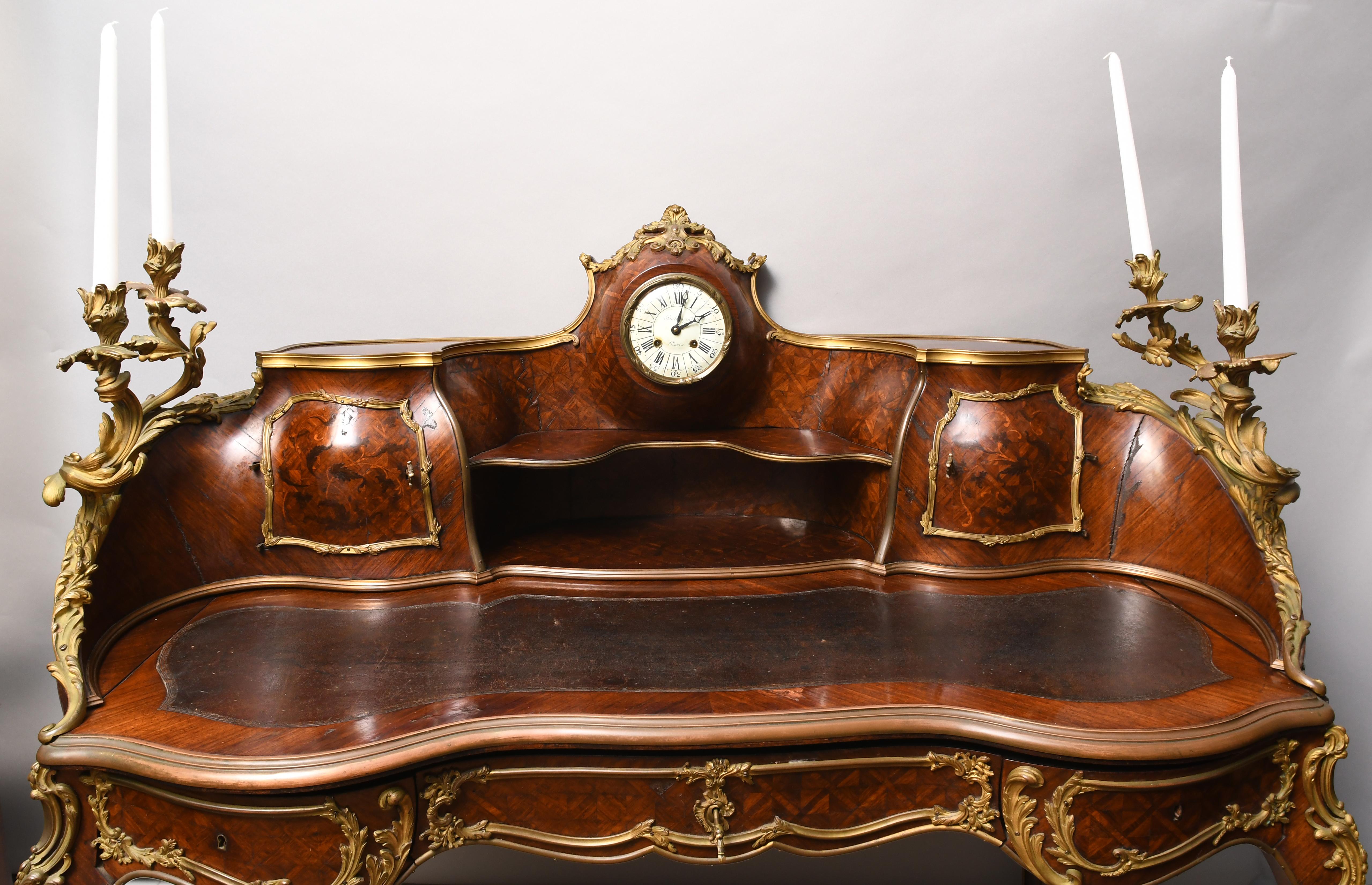 Bureau has four acanthus leaves cast candleholders, leather top desk with two compartments and three frieze drawers. It is supported by four cabriole legs with acanthus leaves scrolling mounts on the knee. The porcelain dial with Roman number signed