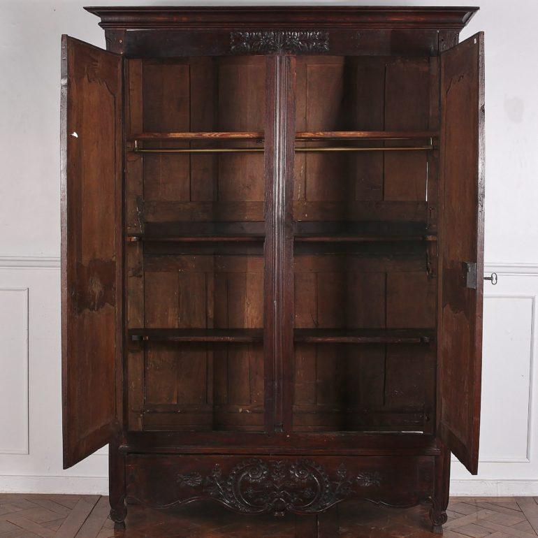 Louis XV-style carved oak two-door armoire, with brass hinges and decorative keyplates. The piece is likely an 'armoire de mariage' or marriage armoire, as it is profusely carved with flowers and baskets of flowers symbolising abundance, prosperity,