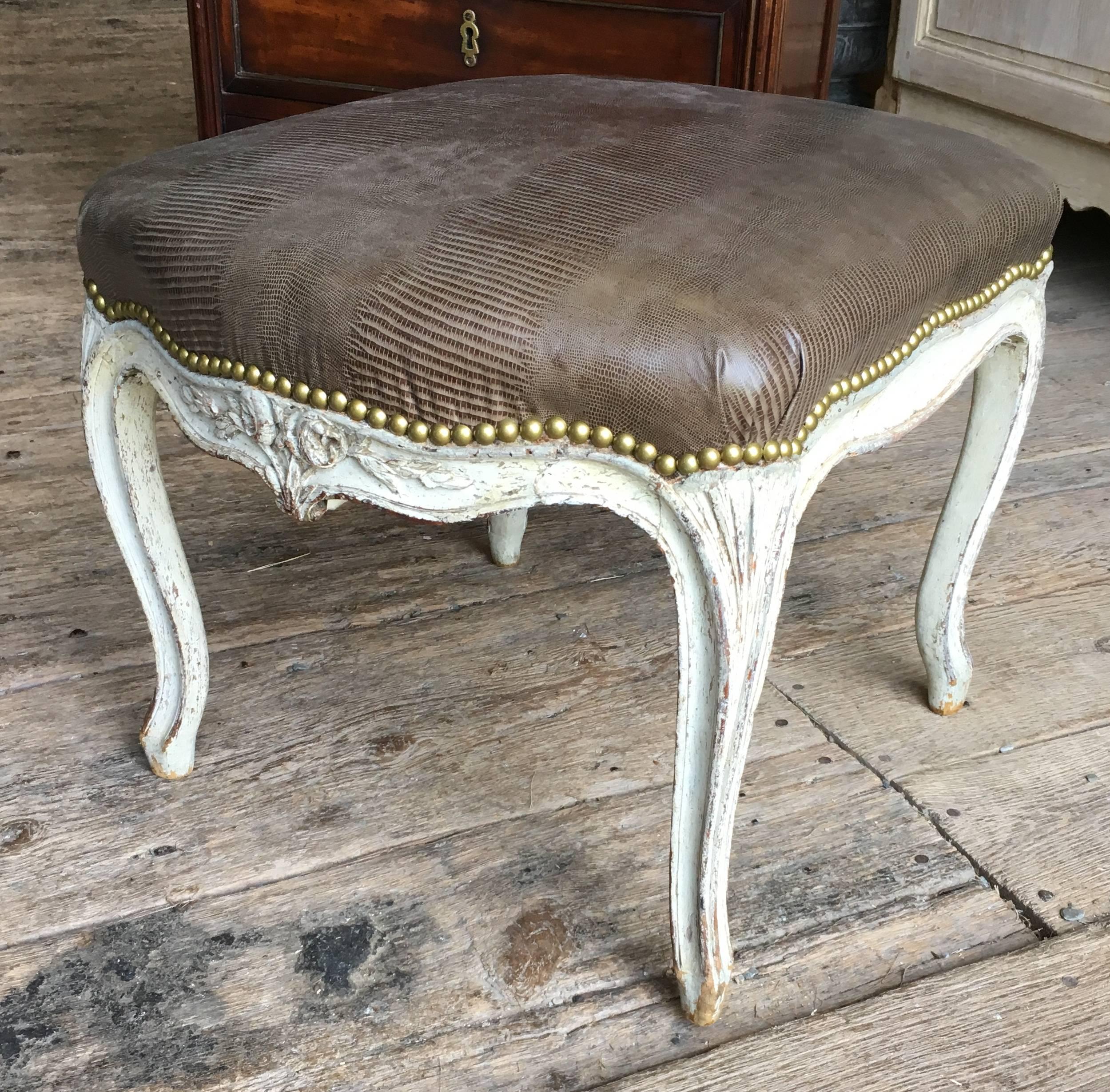 A French Louis XV period tabouret bench in beech, nicely carved with cabriole legs and floral carvings on apron, in old grey/cream painted finish, upholstered in embossed brown leather.