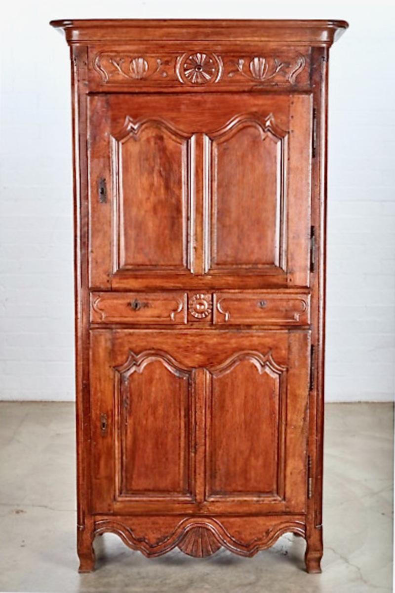 Voici une charmante armoire ou bonnetière en noyer de style provincial Louis XV. Cette armoire présente une configuration peu commune avec deux tiroirs séparant les deux sections de stockage. La bonnetière est ornée de sculptures de fleurs et de
