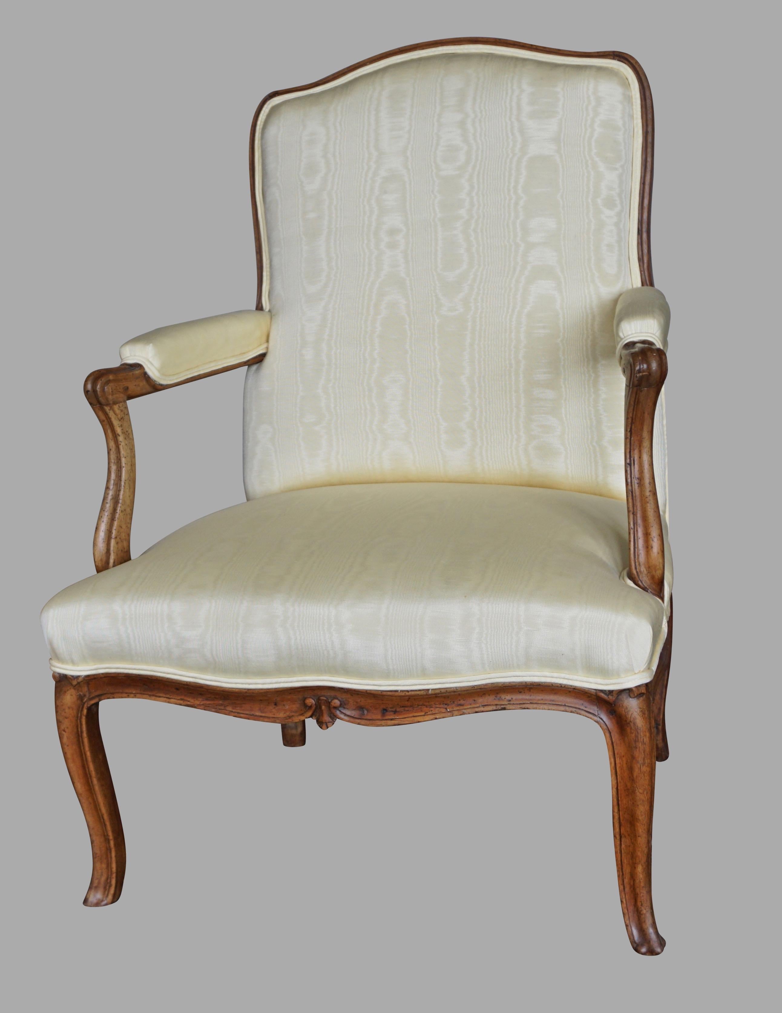 A handsome and generously proportioned French Louis XV period yellow silk upholstered walnut open armchair with a carved front edge. A well-proportioned and comfortable armchair of good scale. Originally with a central stretcher now absent. Circa