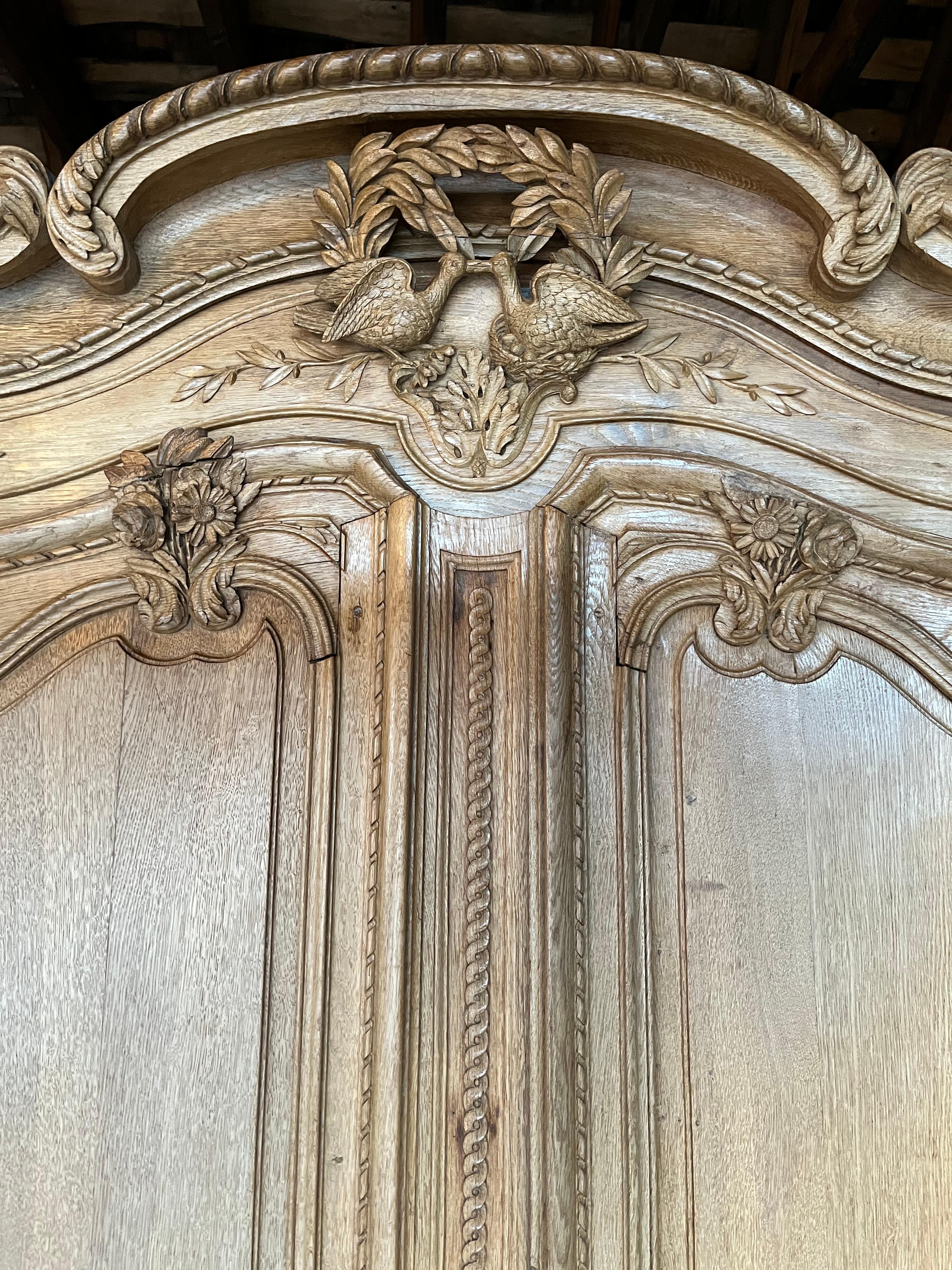 A very nice example of a traditional 18th century Normandy wedding armoire in bleached oak, abundantly carved with garden and floral motifs, with a central bouquet of love birds below the arched cornice. 
The piece retains its original lock and key