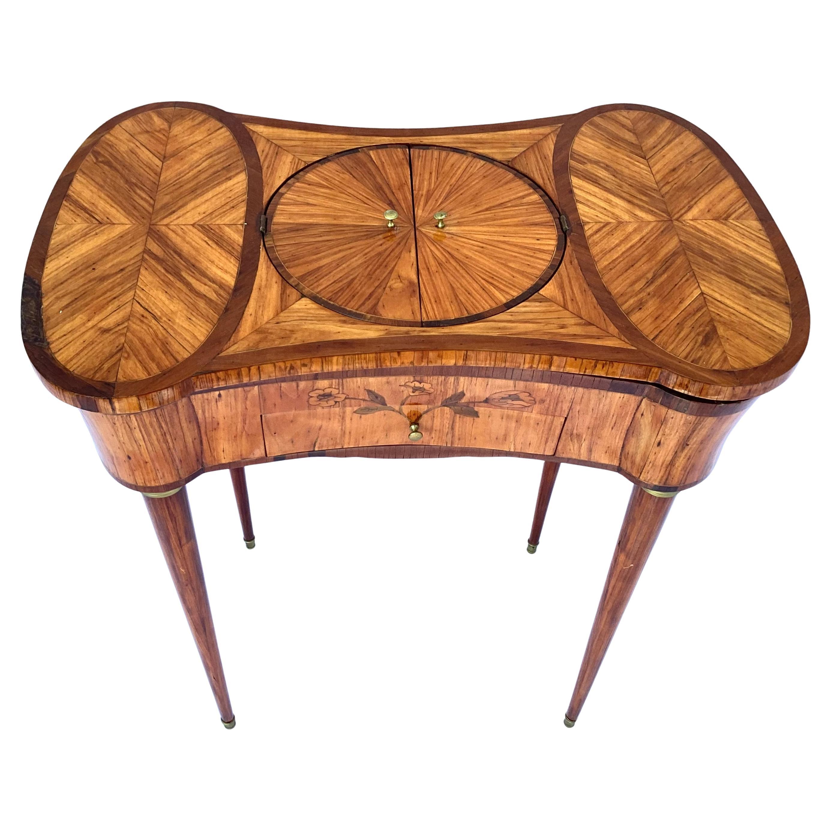Milieu du XIXe siècle Louis XV  Table de travail avec marqueterie. La table comporte un plateau pivotant avec un cercle central qui s'ouvre pour le rangement, ainsi que deux compartiments de rangement de chaque côté lorsque le plateau est tourné. Il