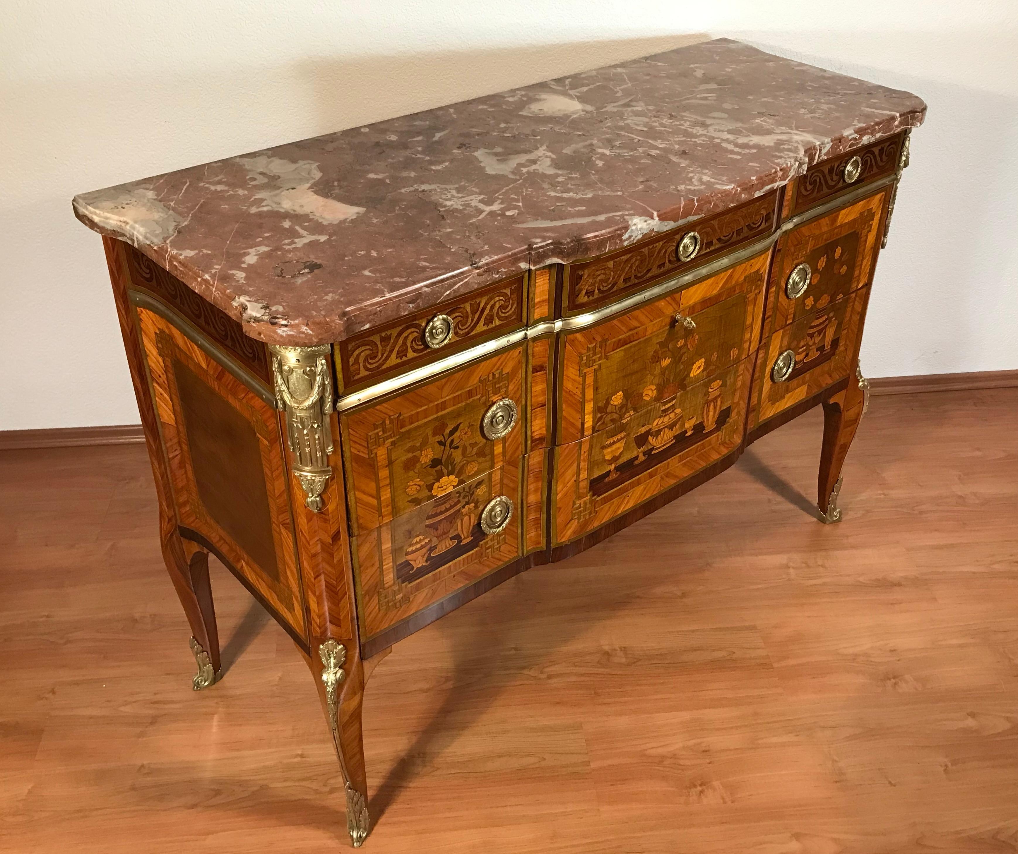 Exceptionnelle commode Transition Louis XV-XVI à cinq tiroirs. La partie supérieure comprend trois petits tiroirs ornés de motifs de vigne finement détaillés, tandis que les deux grands tiroirs inférieurs présentent une élégante marqueterie sans