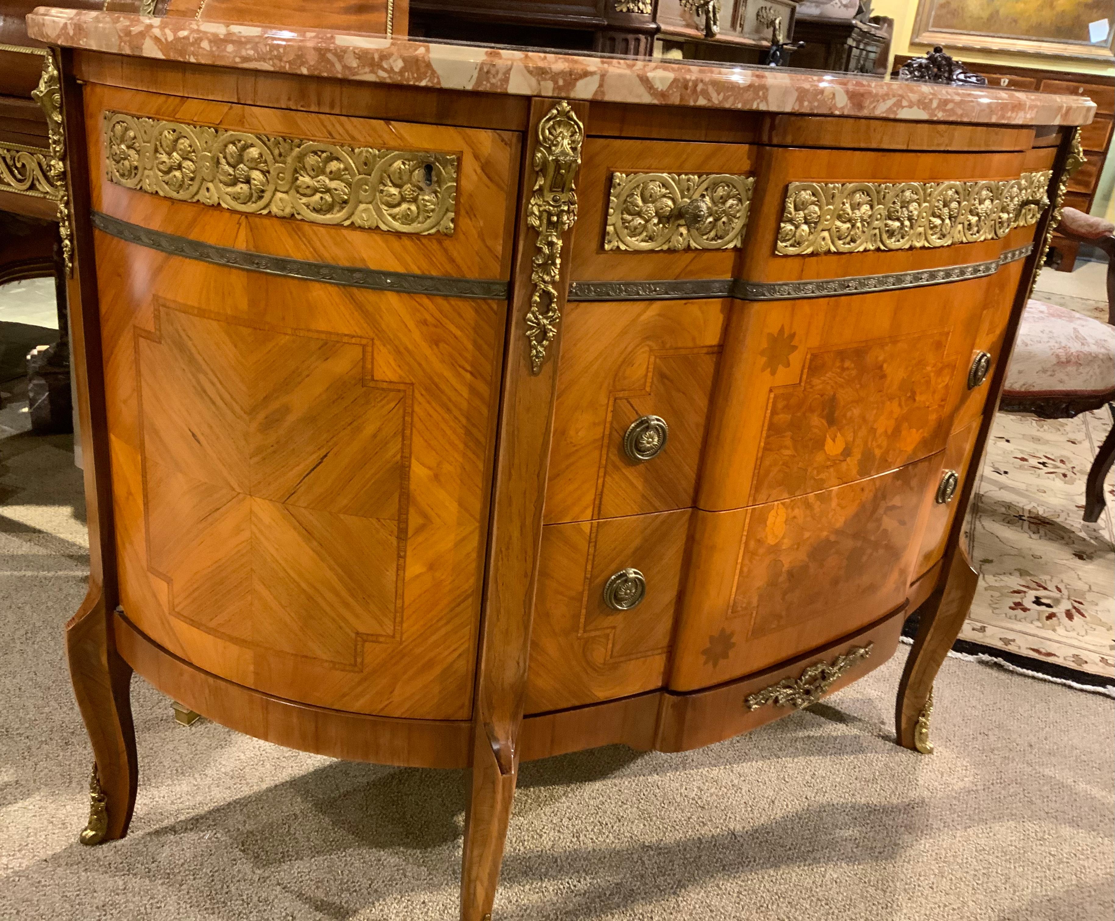 This commode has a bowed shape above a conforming case
Fitted with an ormolu-inset frieze drawer over two long, deep drawers
With a central paneled floral inlay, raised on cabriole legs ending
In sabots. The graceful curved shape of this piece
