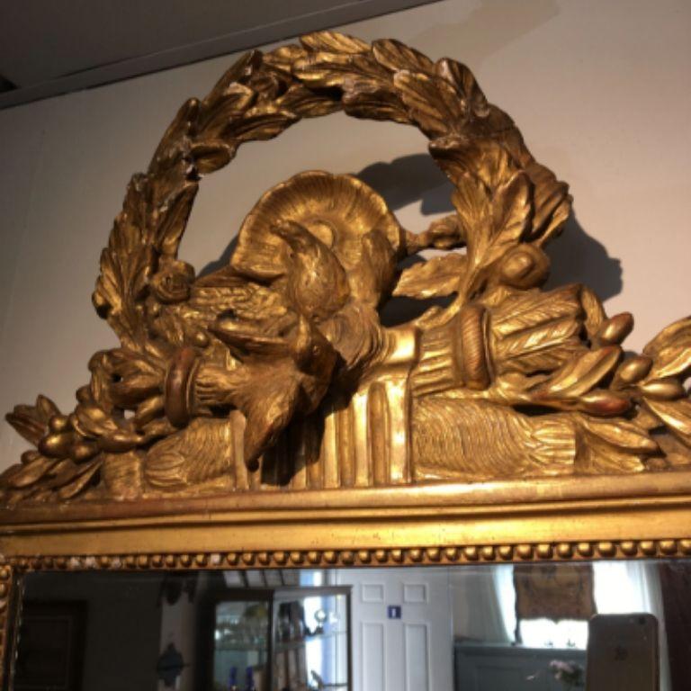 The doves on the crest of this mirror are three-dimensional, carving of the highest quality. Note also the deeply carved wreath and quills and foliate motif. The gilding is original, with the exterior frame of the mirror painted a pale green. The