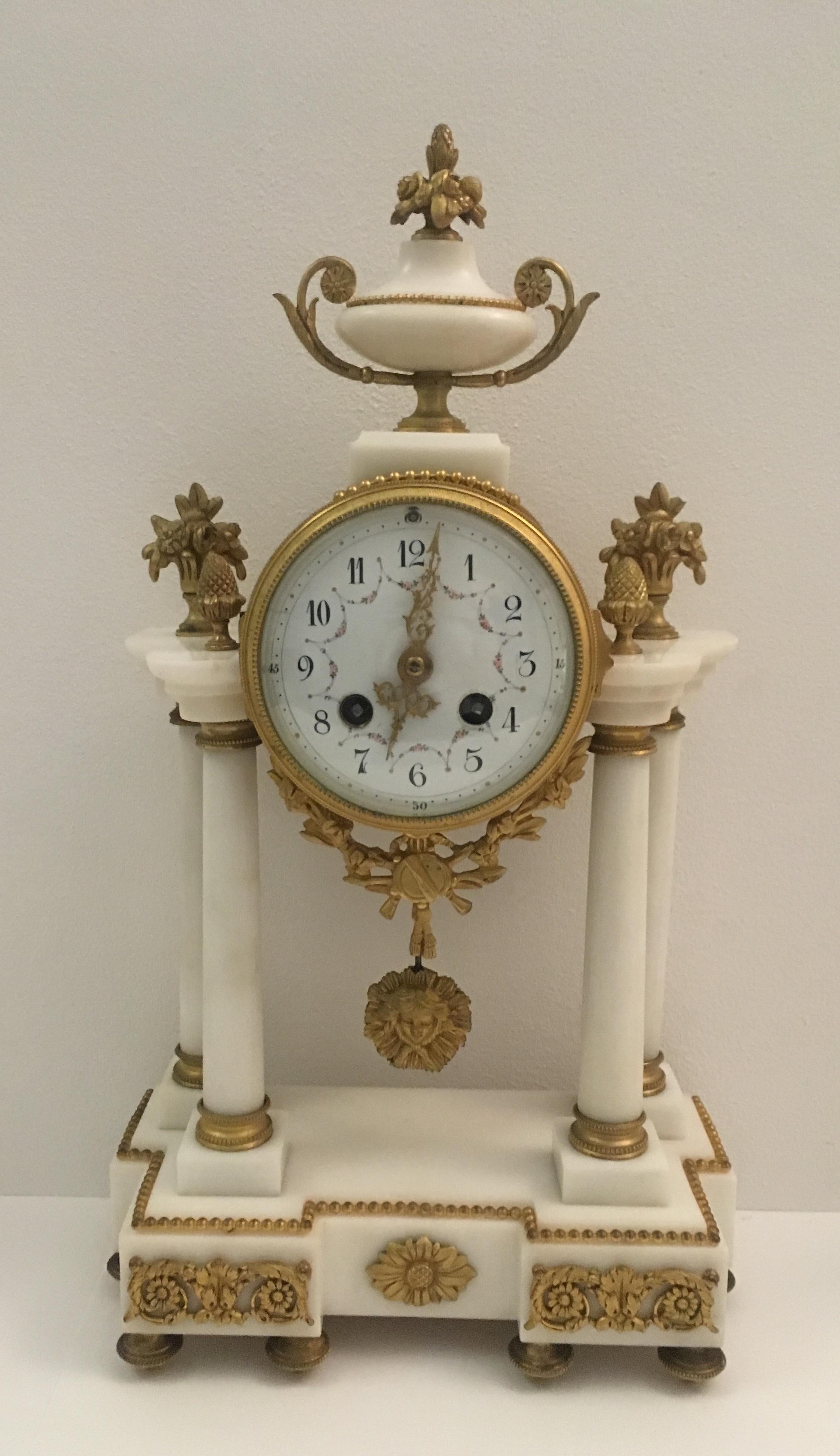 Elegant 19th century French Louis XVI gilt bronze mantel clock and two candelabras in antique white Carrara marble and gilt bronze. The white enamel dial with hands finely worked and gilded, the dial reveals part of the mechanism. The strings of the