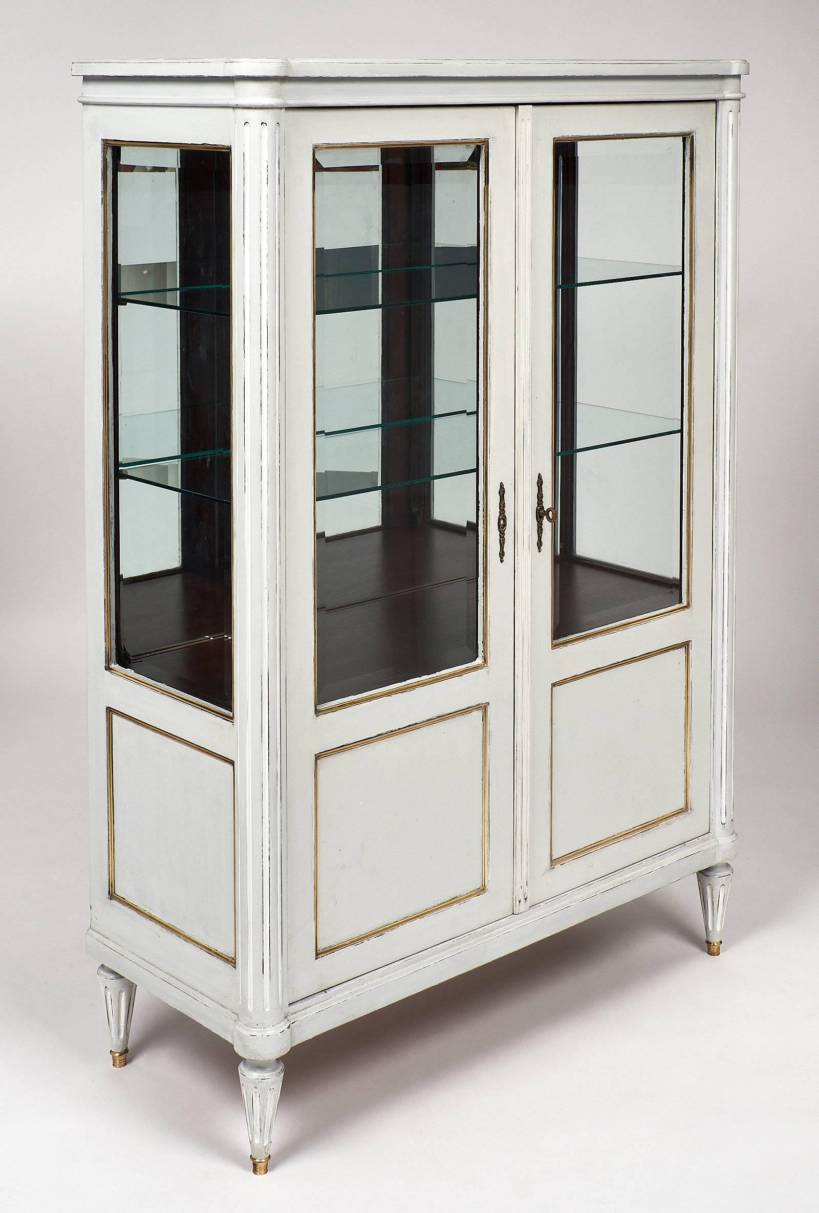 French Louis XVI antique vitrine/bookcase with beveled glass doors and sides. This piece was painted and patinated with a combination of dove gray and white milk paint. Fluted and tapered legs with brass feet and the gilt trims throughout accent the