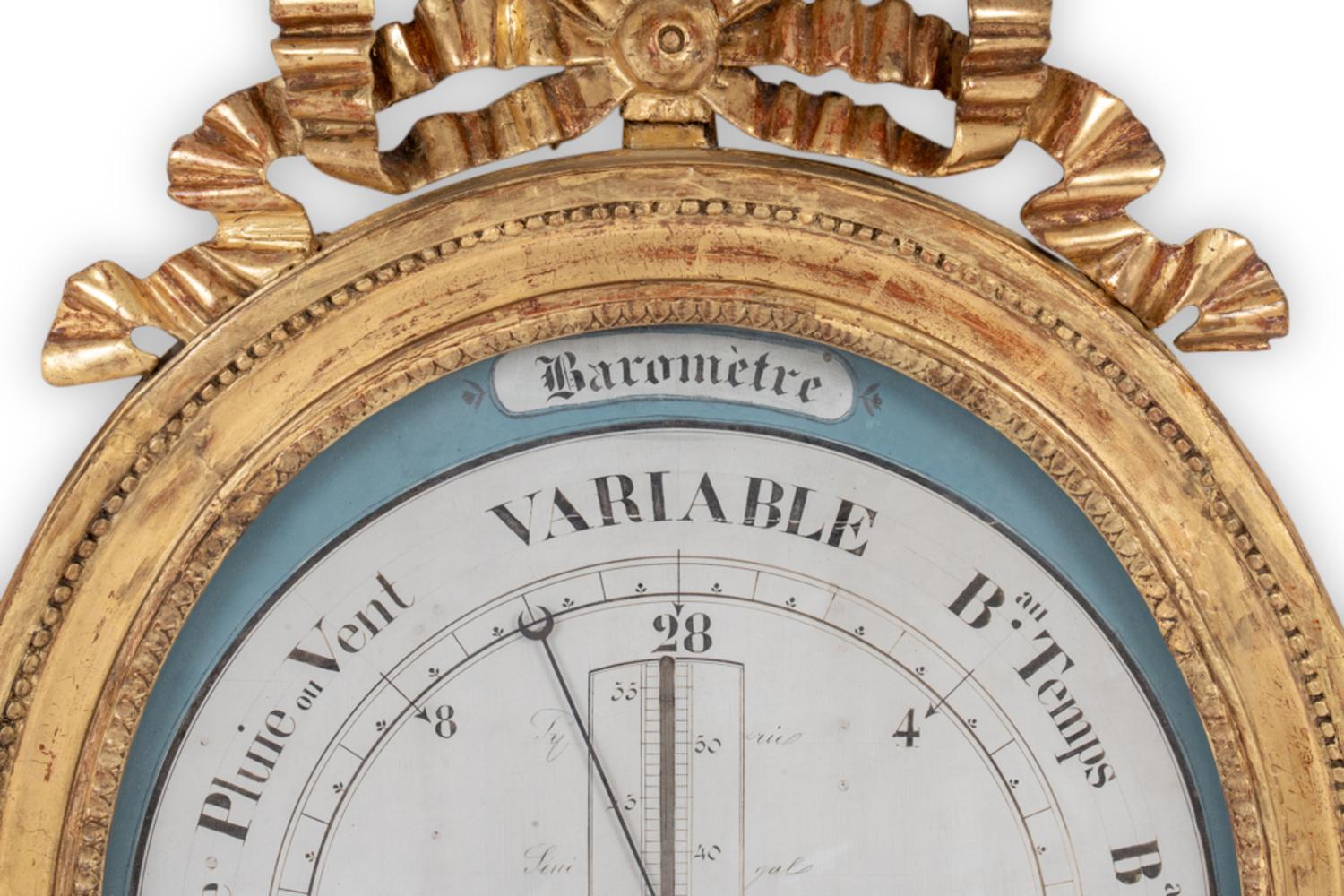 Louis XVI barometer in gilded wood in the shape of a medallion, with a double row of finely beaded decoration. It is topped with a pediment decorated with a knot-shaped garland. The metal hand indicates time variations on a white and blue