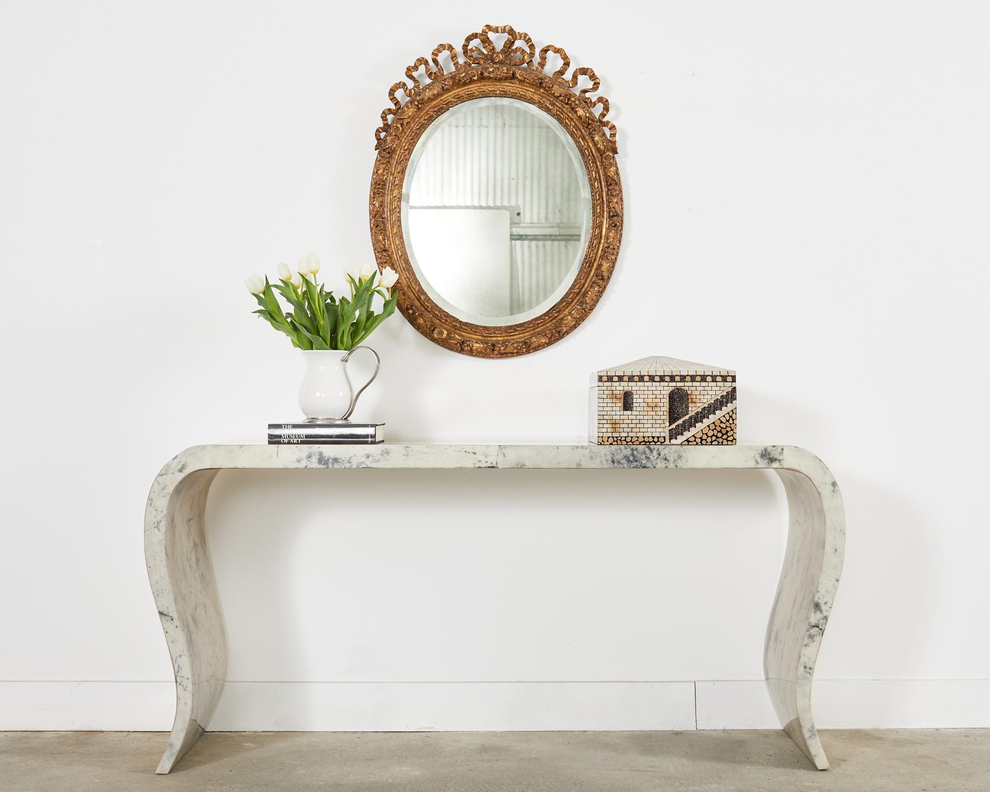 Gorgeous 19th century Italian carved wall mirror made in the grand Louis XVI taste having a baroque style carved frame. The giltwood frame is embellished with oak leaves carvings in an oval form. The frame features a large ribbon finial bow with
