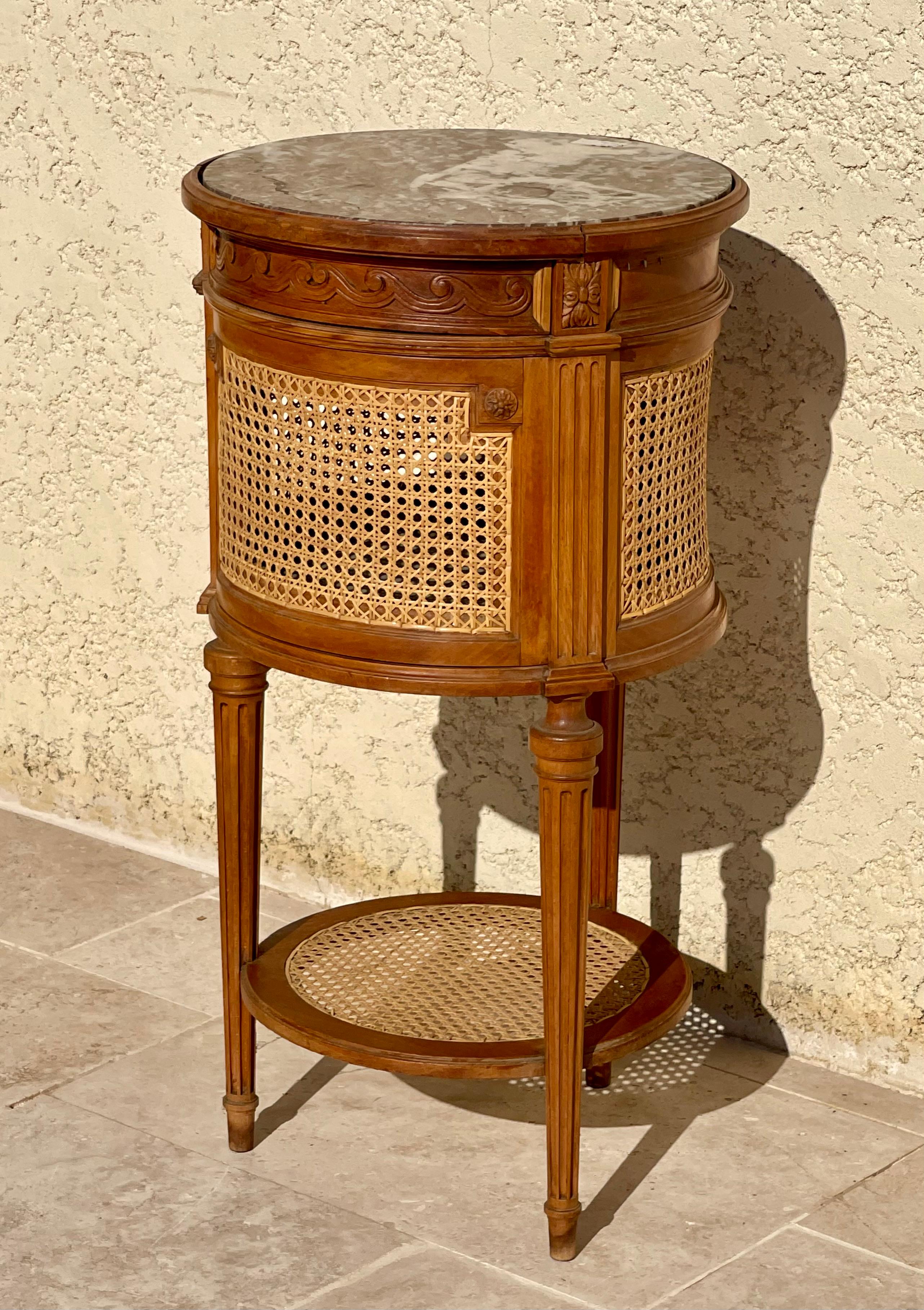 Chevet de style Louis XVI en noyer et rotin en forme de tambour. Il s'ouvre par une porte arrondie et possède un plateau en marbre. Travail français parisien vers 1900.

Dimensions
Hauteur 80cm
Diamètre 42cm