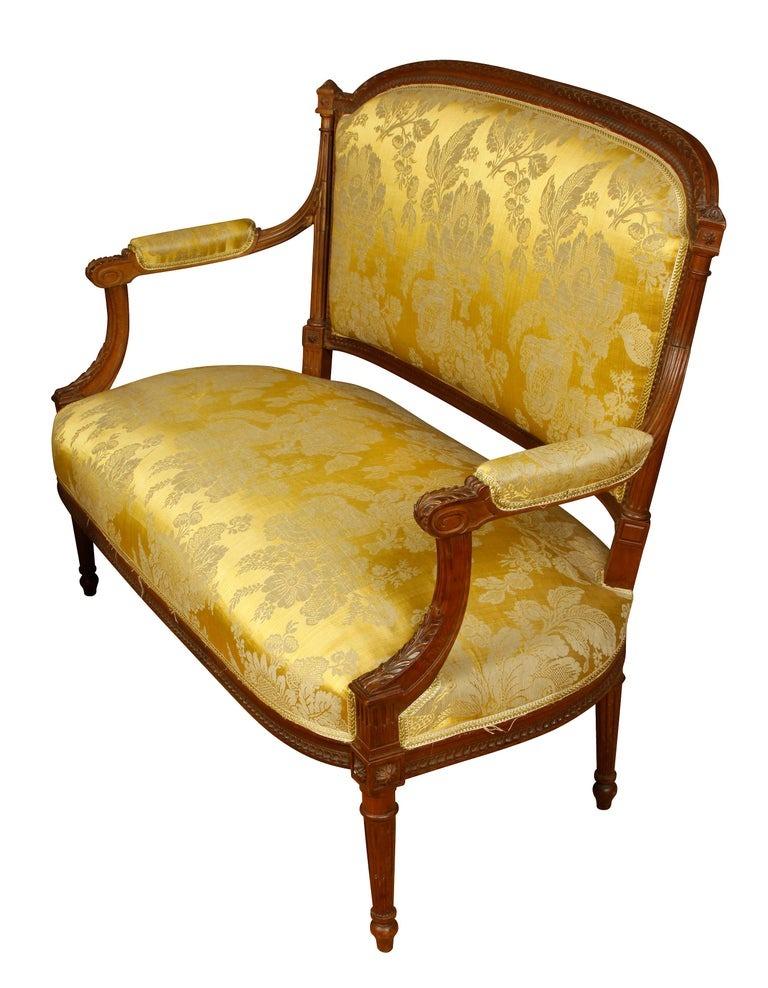 Louis XVI beechwood settee in gold tone on tone damask silk with carved arms and legs. Beautiful workmanship to the frame is evident in the intricate carvings throughout, with floral and leaf detail. The silk fabric is a luxurious quality. The