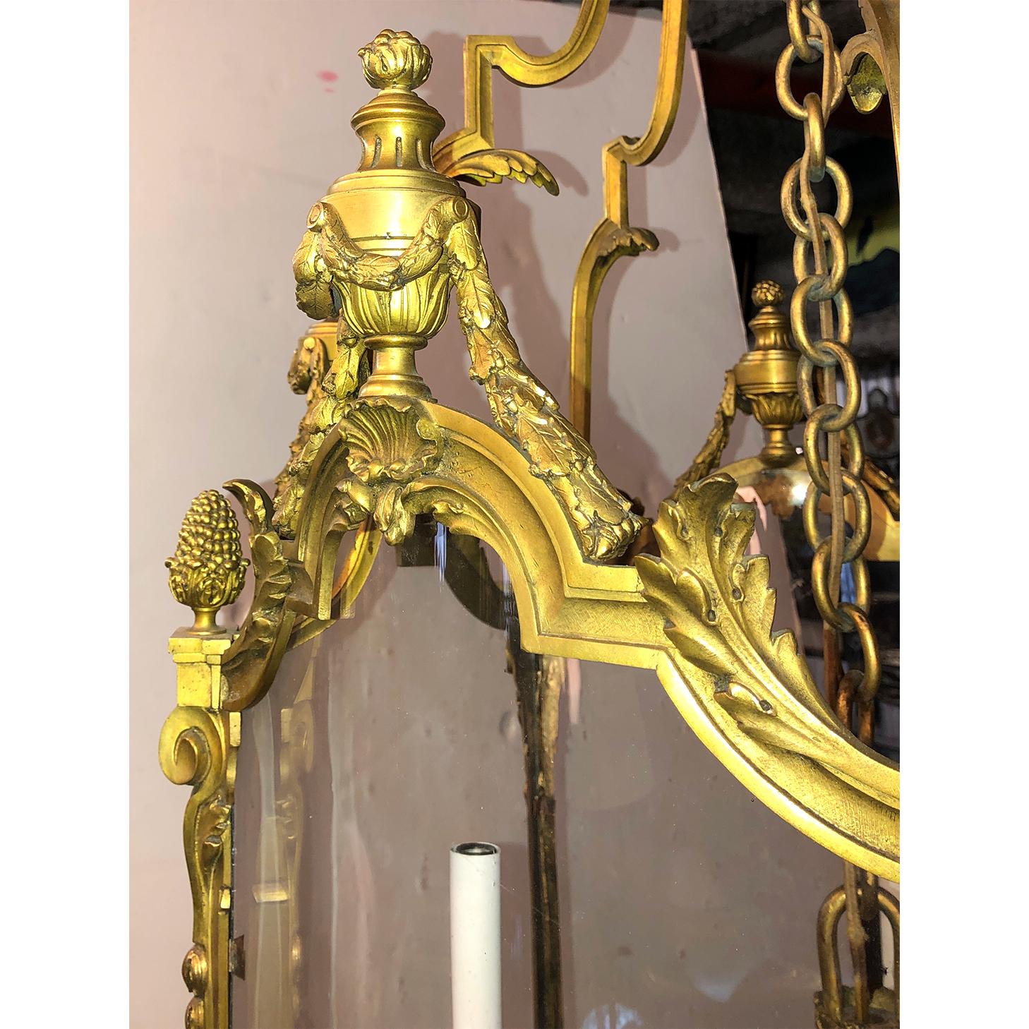 Fina linterna de salón francesa Luis XVI de bronce dorado y tres brazos, con lados serpentinos, guirnaldas de bronce, urna de llamas para remates, bellotas y adornos de hojas de acanto.