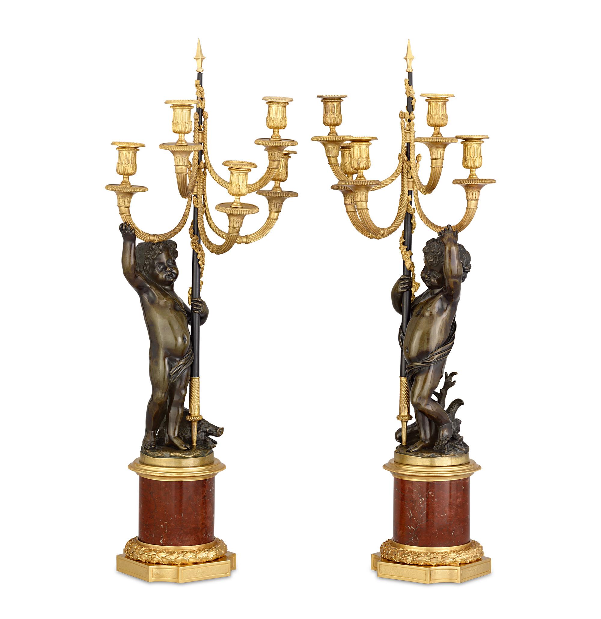 Squisitamente realizzati in bronzo ormolu, questi rari candelabri gemelli mostrano la grandezza neoclassica dello stile Luigi XVI. Due putti in bronzo spazzolato che reggono lance sostengono le strutture a cinque luci, mentre la testa di cinghiale e