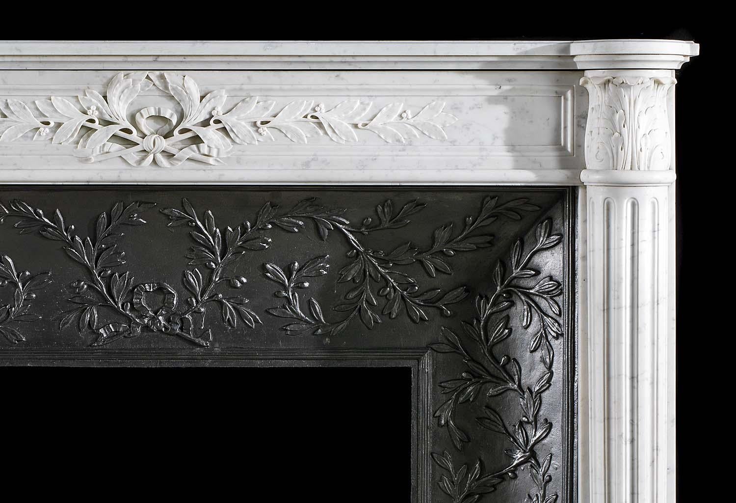 A small French Carrara marble antique fireplace surround in the Louis XVI style with its original ornate cast iron insert. The frieze, centred by a finely carved laurel wreath trailing sprays of laurel to ether side, is flanked by acanthus adorned