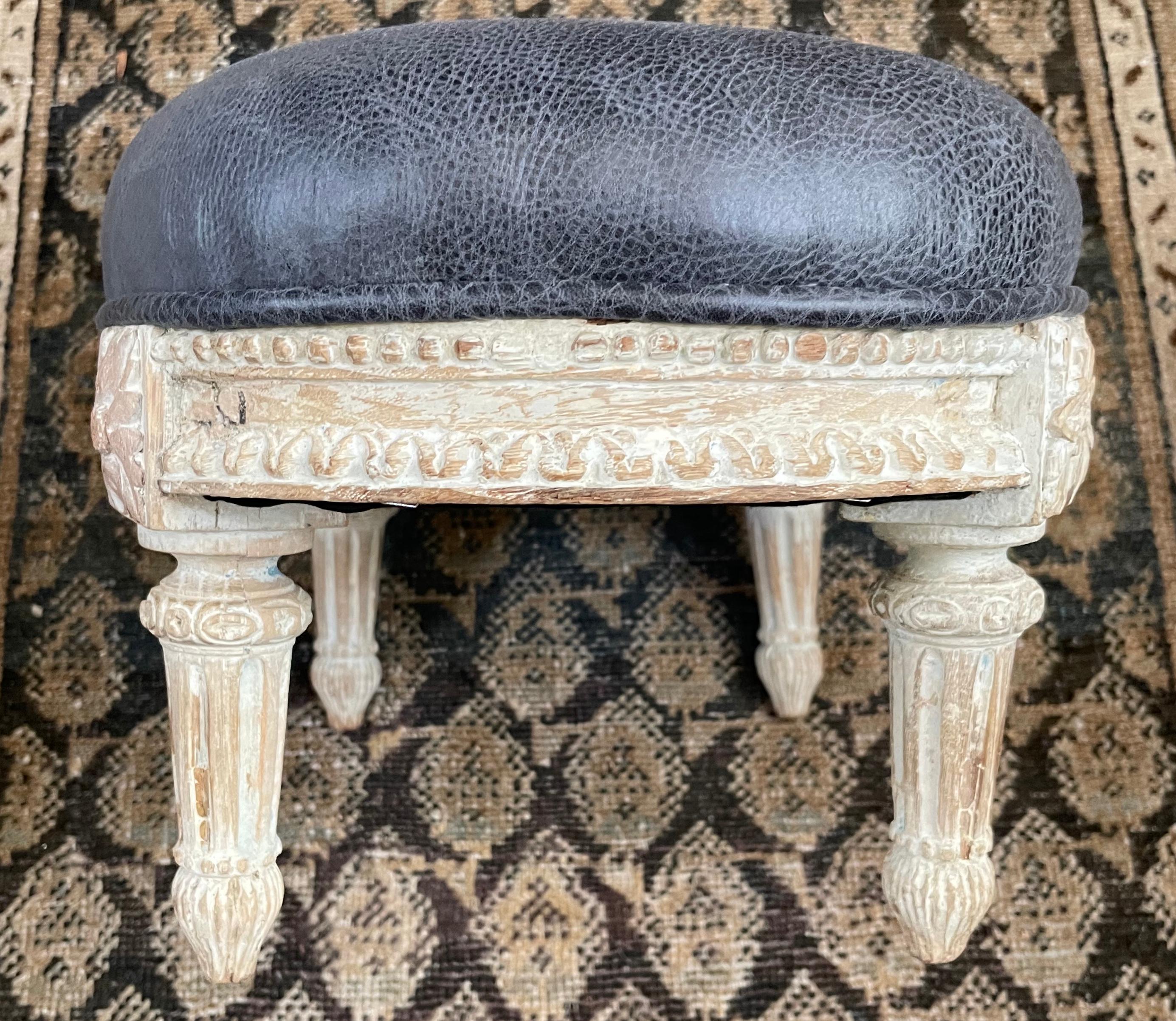 Louis XVI carved stool. Neoclassical Louis XVI period carved bleached white oval footstool with bead banded rim; foliate blocking above flute carved tapering legs, newly reupholstered in blue grey leather. France, early 19th century. 
Dimensions: