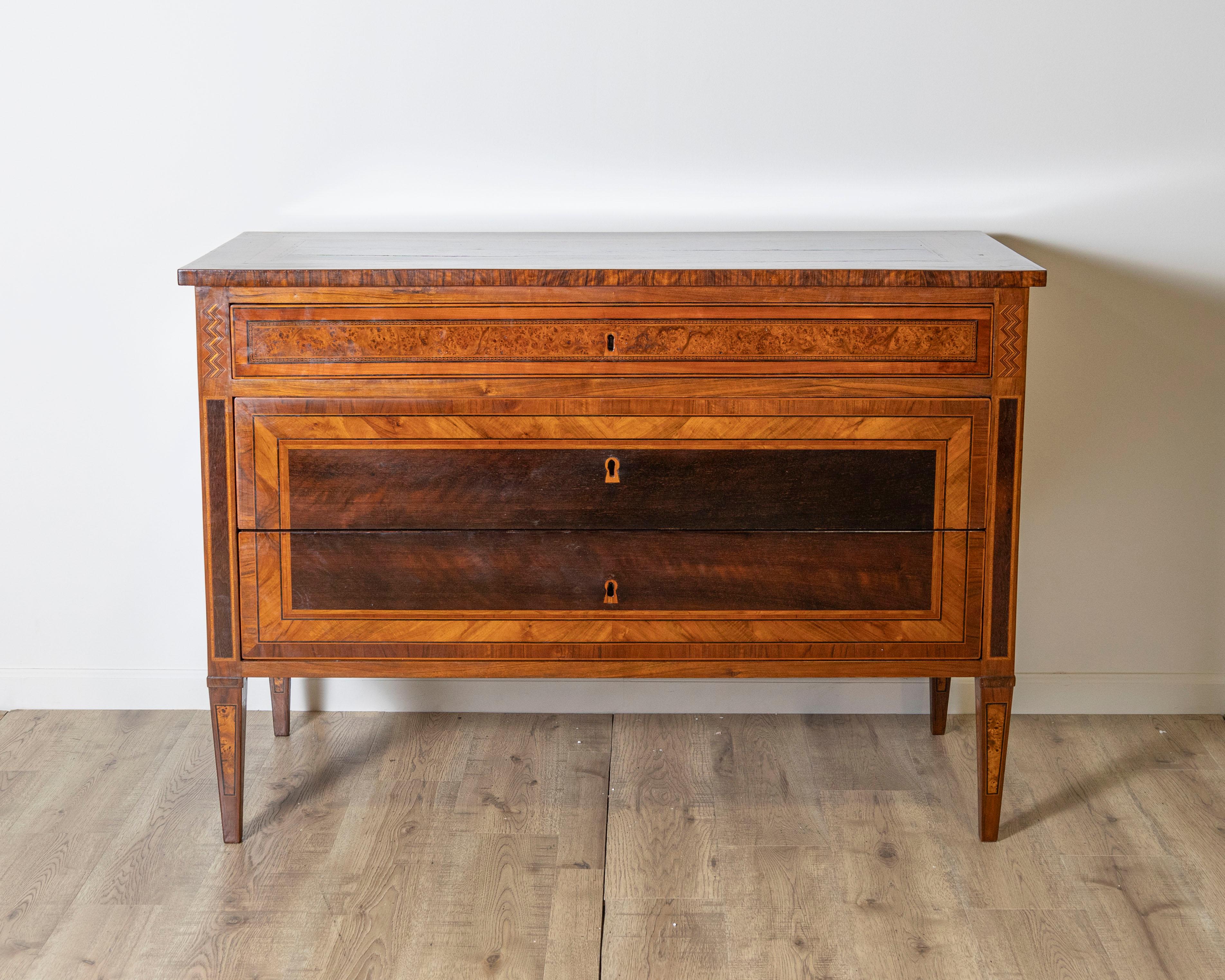 A refined Louis XVI period chest of drawers from Bologna, Italy, crafted in the late 18th century and richly inlaid in a harmonious blend of walnut, olive, maple, and ebony. This elegant piece is a testament to the superior craftsmanship of Emilian