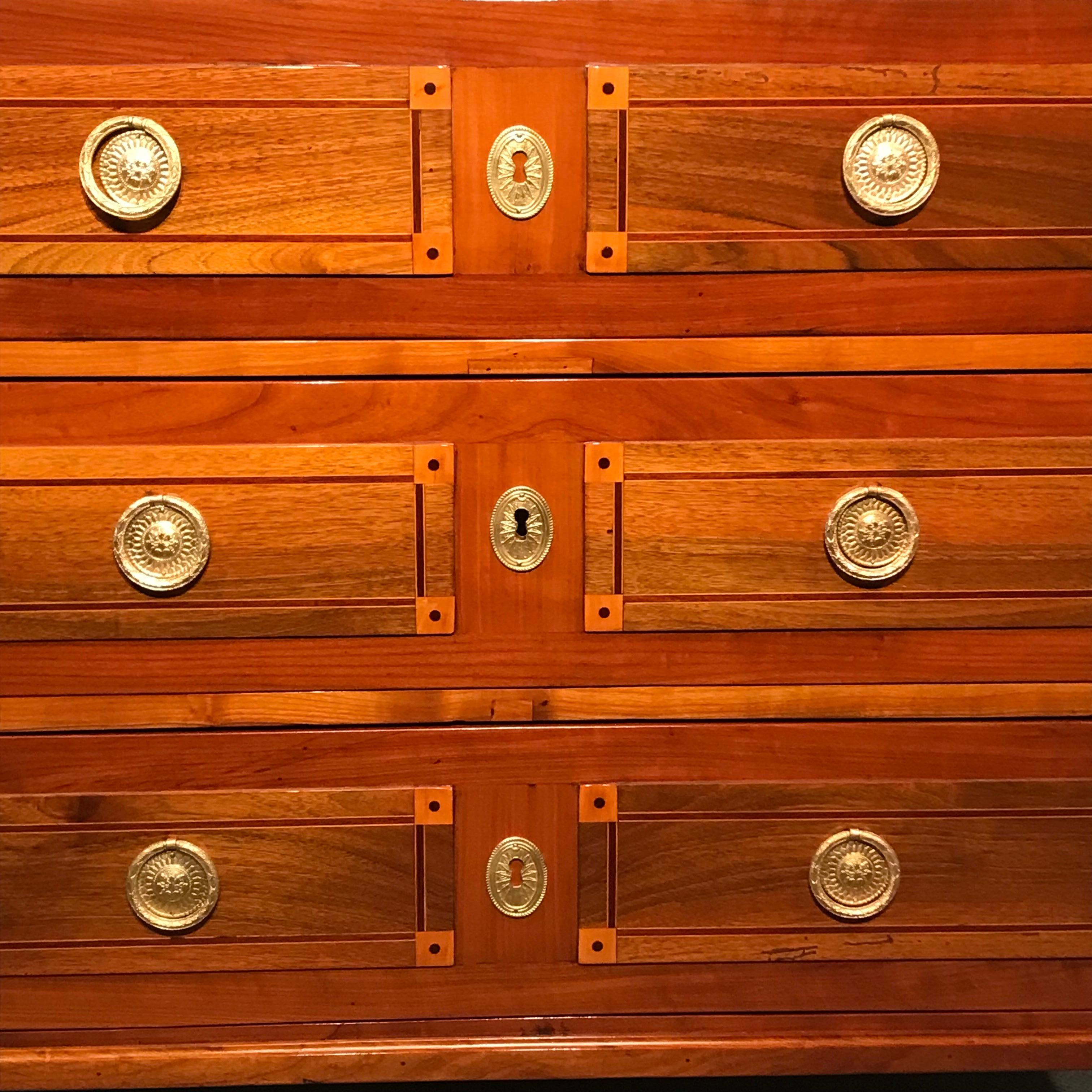 This unique Louis XVI Chest of drawers dates back to 1780 and comes from Southern Germany. The three drawers commode has a pretty cherry veneer with elegant, geometric inlays on front, top and sides. Additional hand carved motifs embellish the