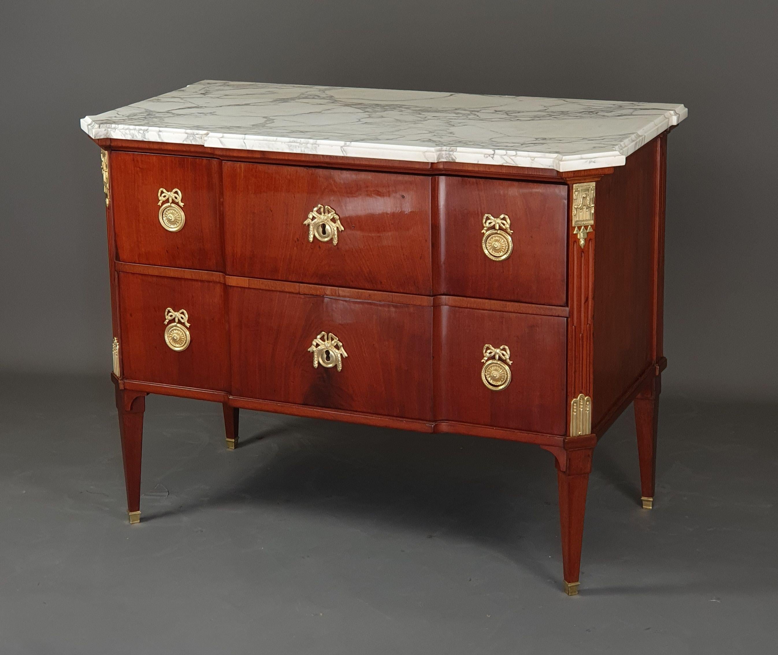 Elegant Commode from the Louis XVI period in blond mahogany veneer with beautiful ornamentation of gilded and chiseled bronze.

Central projection, front uprights with a cutaway adorned with rudent grooves, also projection on the rear uprights