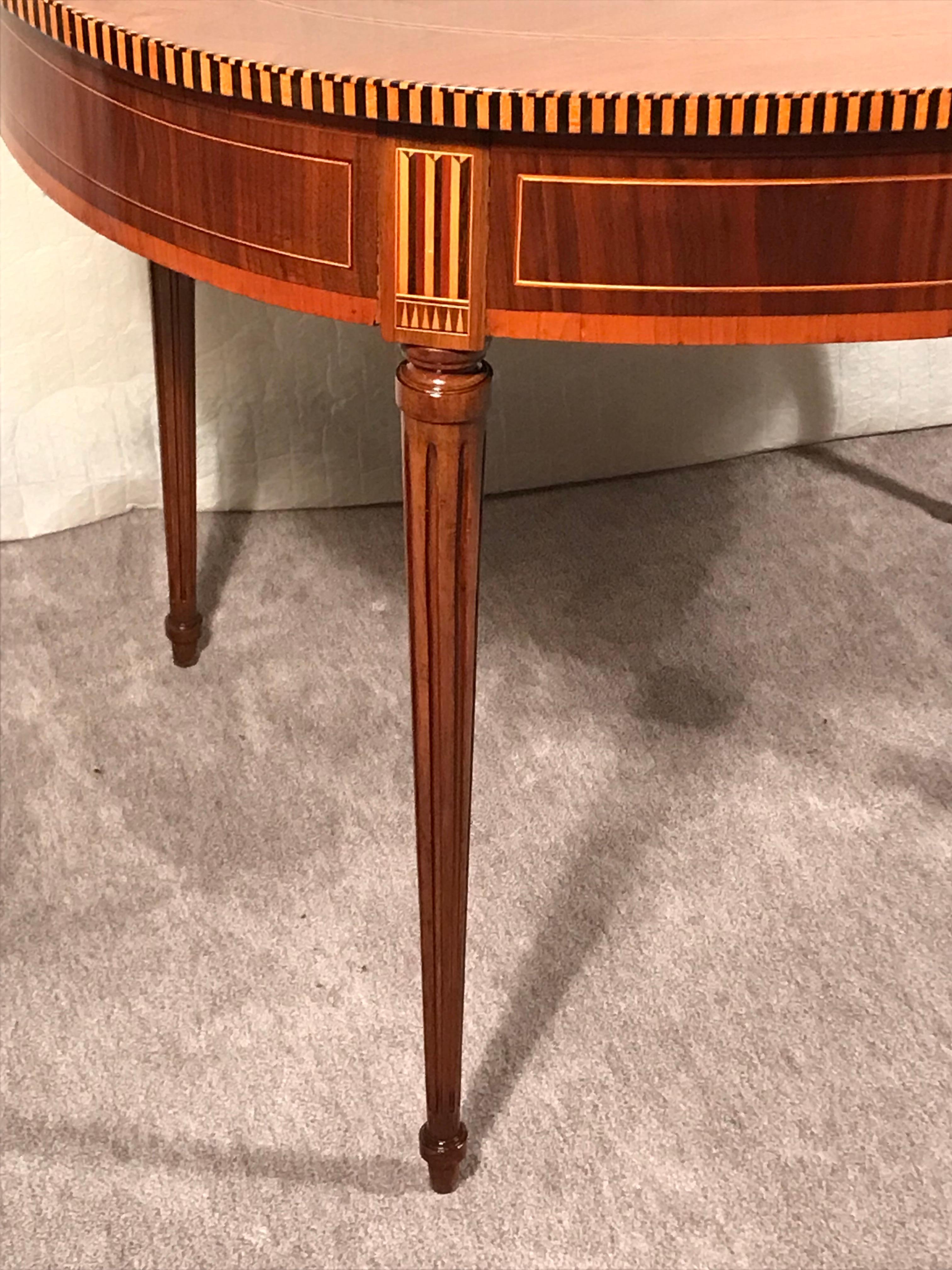 This original Louis XVI dining or center table dates back to 1780-1800. The oval table stands on four fluted legs and has a beautiful walnut veneer. The apron and the top of the table are additional decorated with intarsia. The table comes