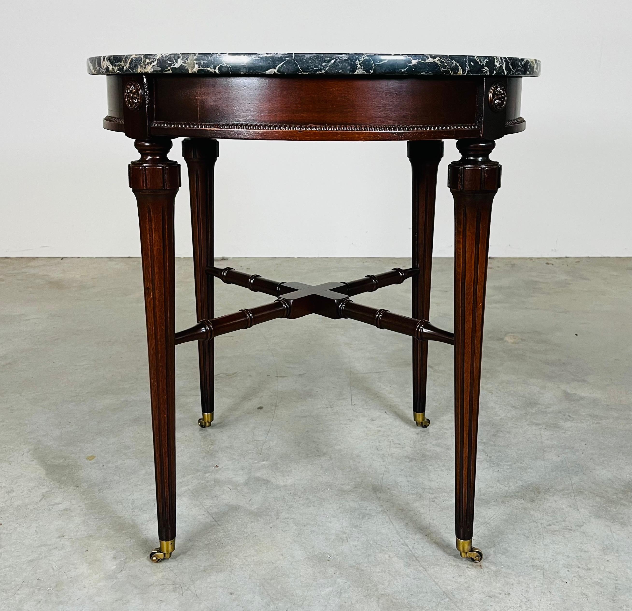Guéridon en acajou sculpté de style Directoire français avec marbre italien Nero sur un cadre en acajou sculpté de style Louis XVI orné d'écussons floraux sur des pieds sculptés reliés par un support en X en faux bambou et des roulettes en laiton