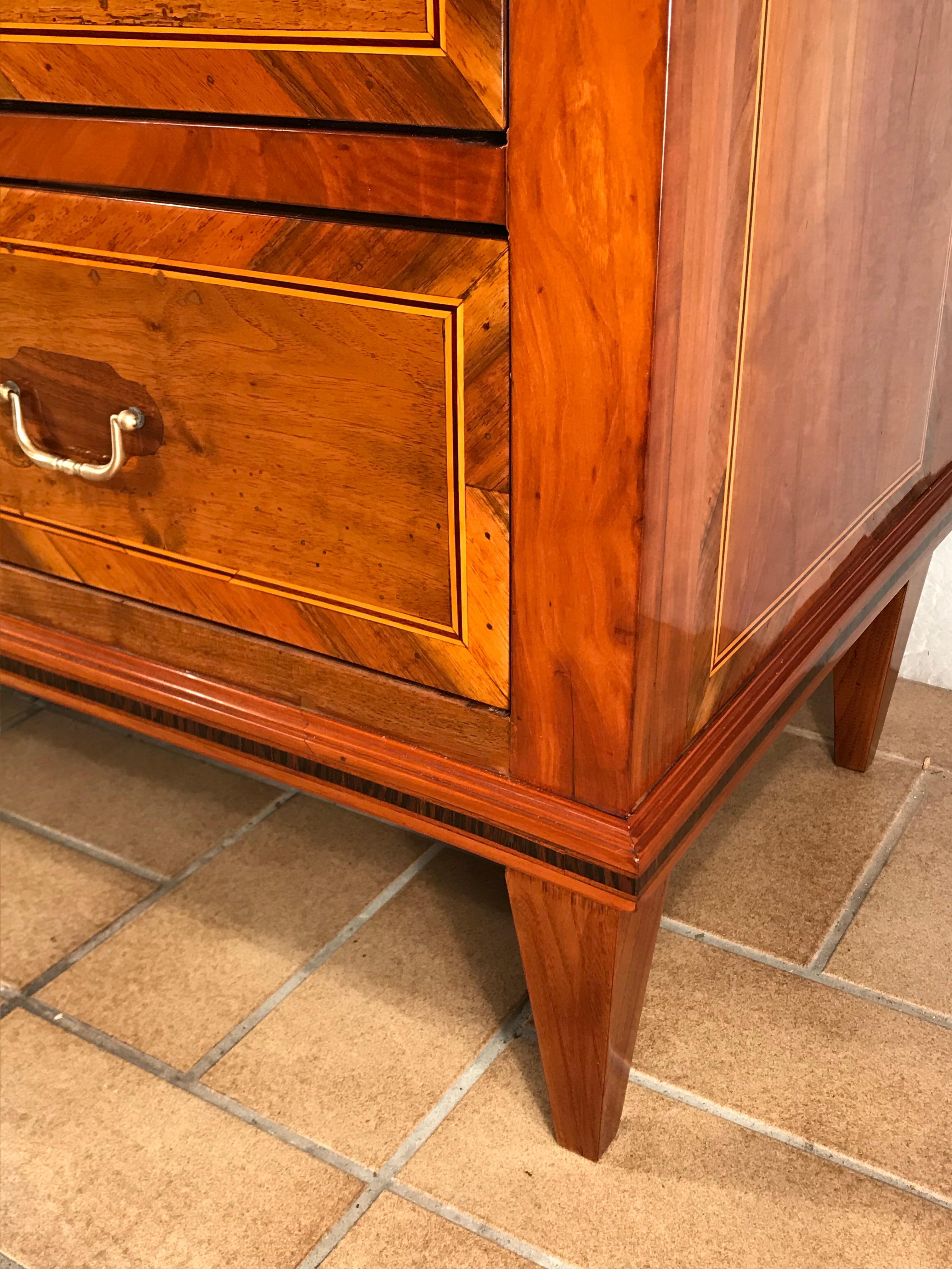 Commode Louis XVI, Allemagne du Sud 1780.
Cette commode Louis XVI originale du XVIIIe siècle comporte trois tiroirs et repose sur quatre pieds carrés effilés.
Il est agrémenté de magnifiques placages en noyer et en cerisier. Les différents champs de