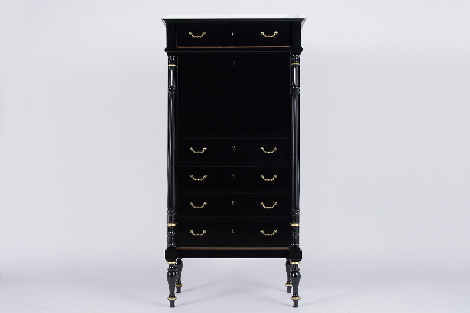 This ebonized Louis XVI style secretaire has been completely restored and been stained in a black lacquered finish with gilt details. It also features a white marble top, single top drawer, four large drawers with two brass handles each and a