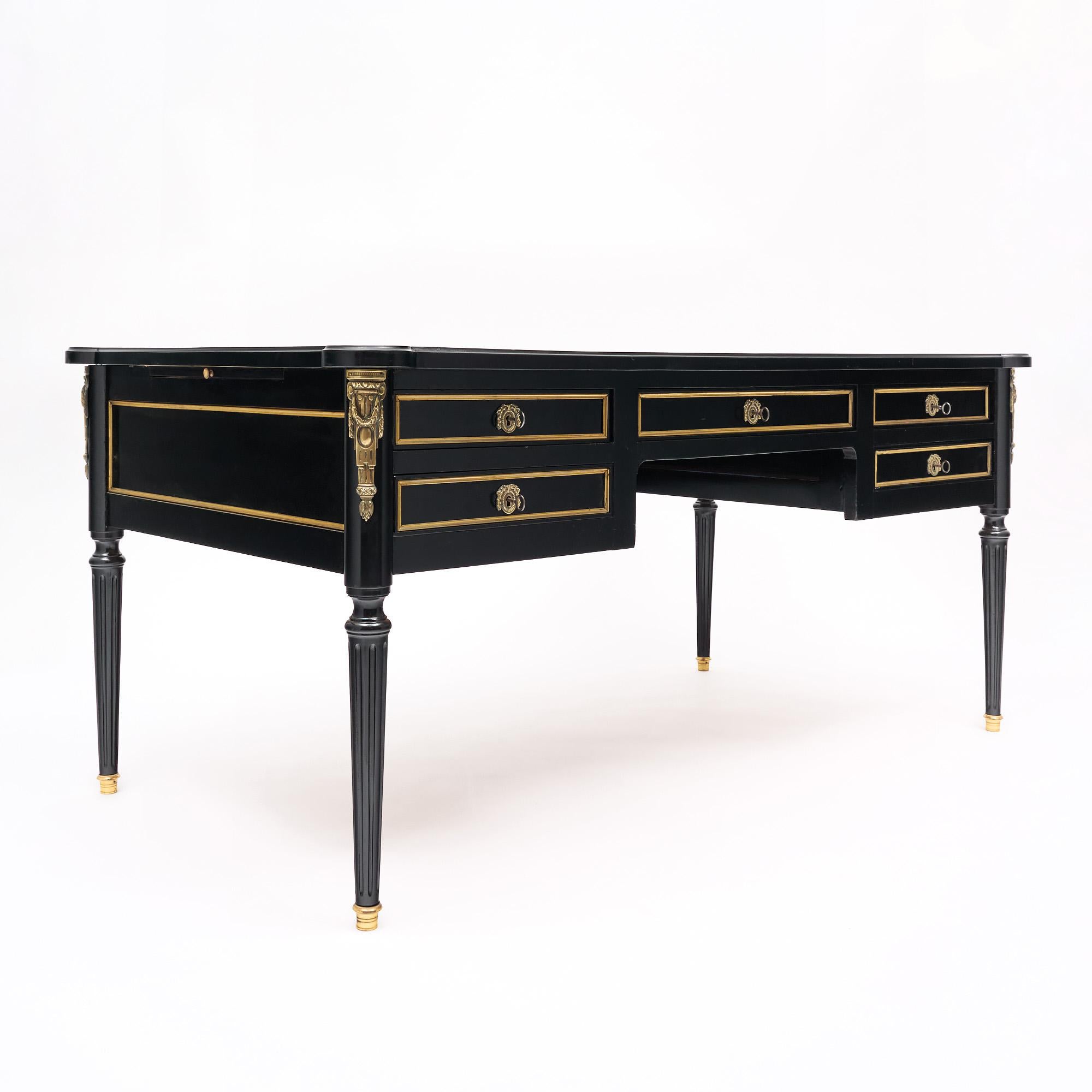 French Louis XVI style desk made of solid wood construction, primarily mahogany. It has been ebonized and finished with a lustrous French polish of museum quality. The table is covered in gilt brass trim and décor throughout. It is supported by