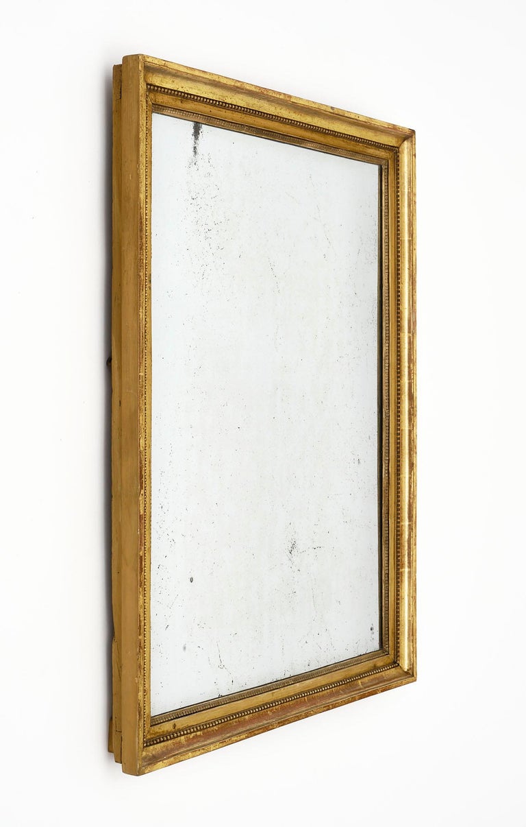 French mirror with original mercury mirror surrounded by a beautiful hand-carved Louis XVI style frame. We love the pearled texture to the beading and the lovely detail of this antique piece. The terra cotta coloring shows through the gold leaf,