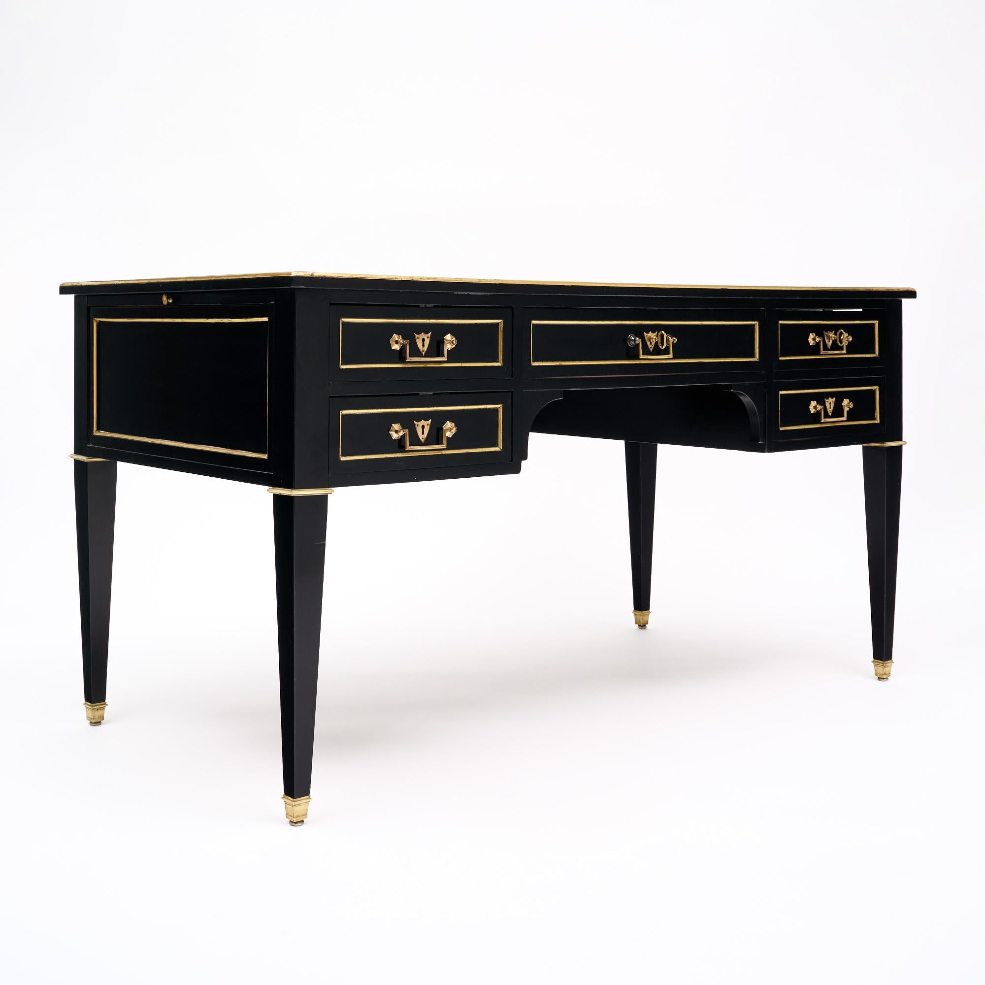 French Louis XVI style desk made of mahogany that has been ebonized and finished with a lustrous museum quality French polish. The writing table is trimmed with gilt brass throughout, and the tapered legs are capped with gilt bronze feet. Four