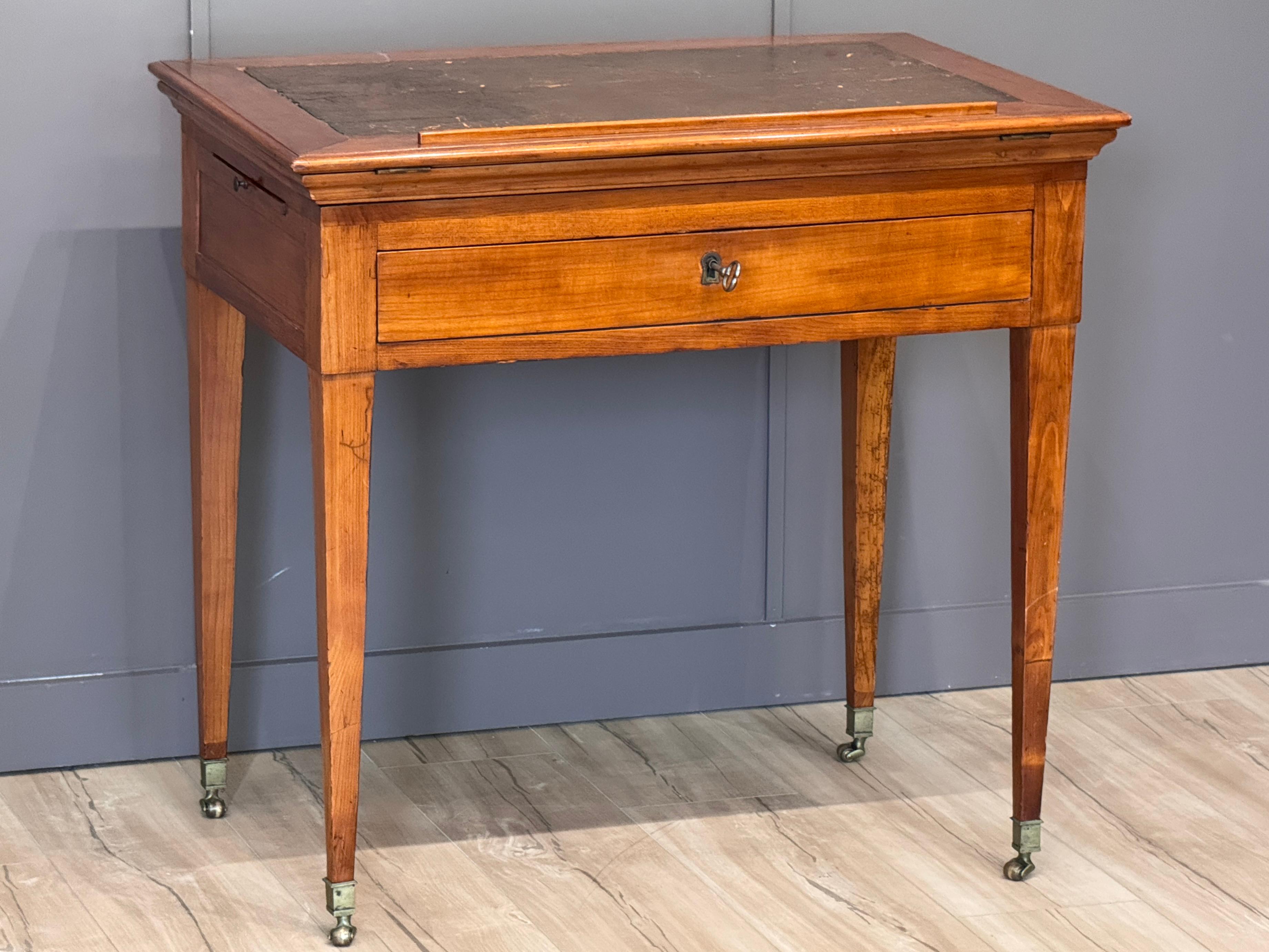 A Louis XVI period French architect’s table in fruitwood with an adjustable leather-inset drafting top. The table features a single drawer, slide-out candle supports, and classic tapering legs on casters. Finely crafted with brass hardware and