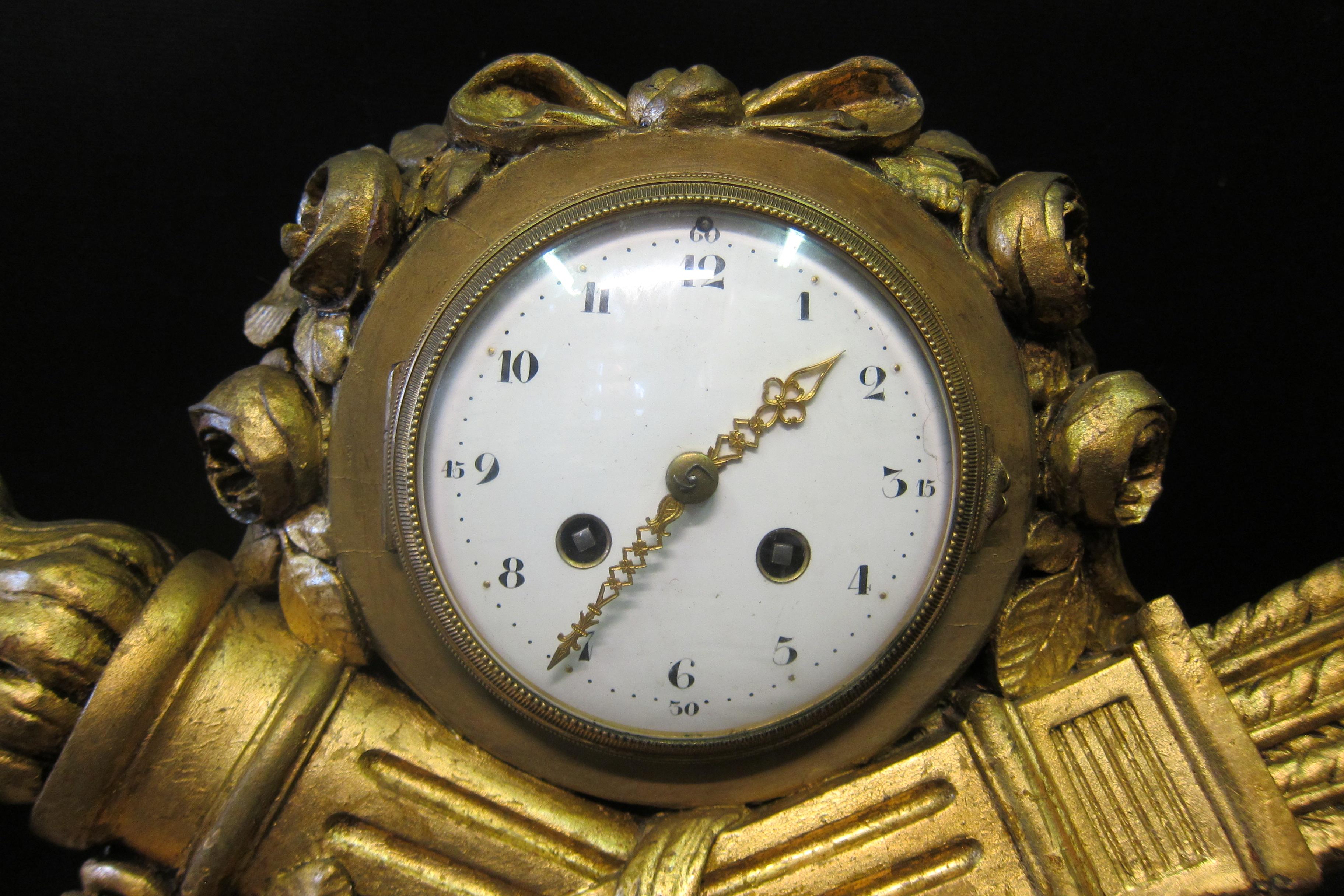 Cette belle horloge de cheminée française Louis XVI en bois doré date de la fin des années 1880. L'horloge est conçue avec des symboles sculptés détaillés d'une torche enflammée croisée avec un carquois de flèches. De plus, on trouve une vigne de