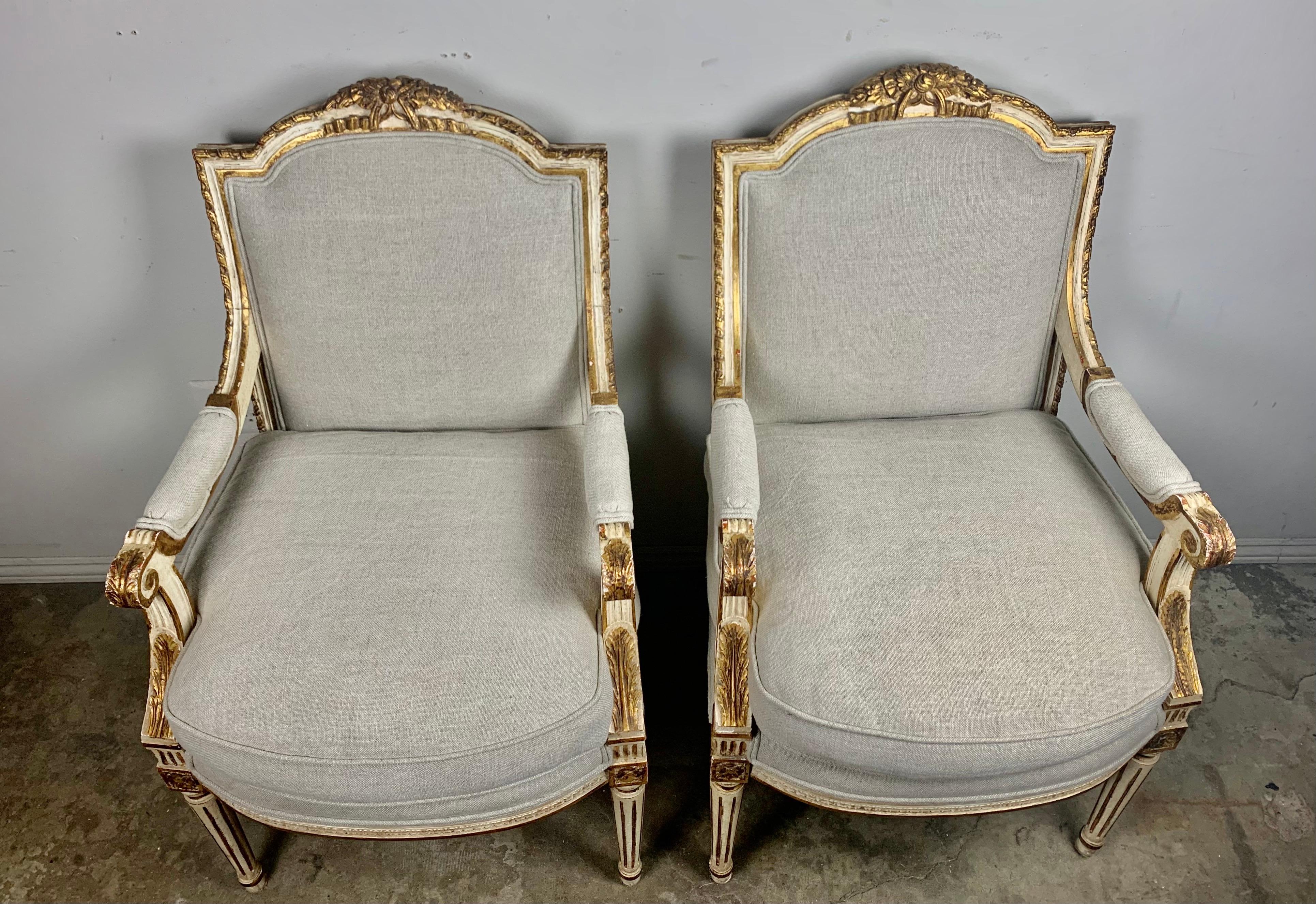 Pair of French Louis XVI painted and parcel-gilt armchairs standing on four straight fluted legs. The armchairs have 22-karat gilt carving throughout. The armchairs are newly upholstered in a washed Belgium linen with loose down filled cushions.