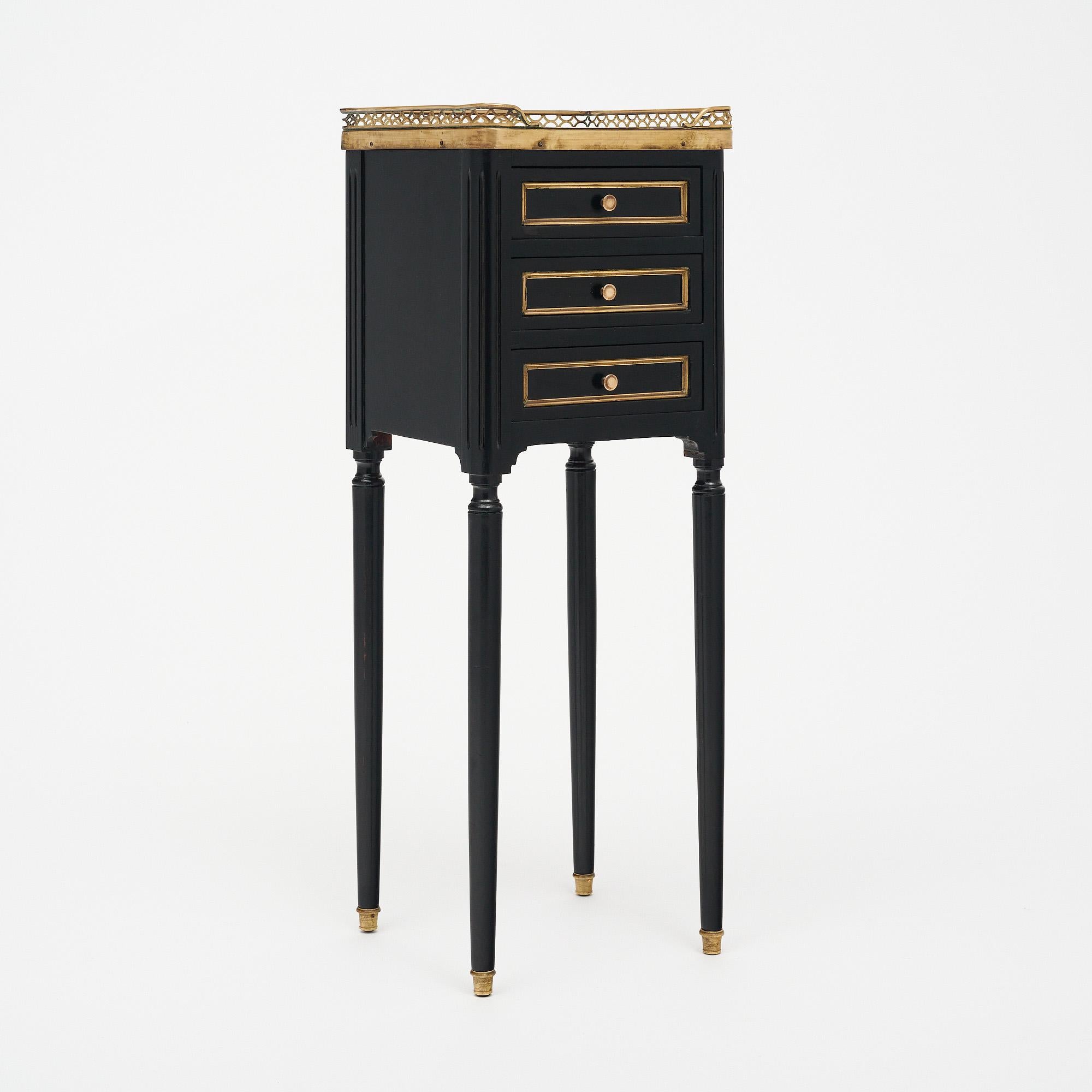 Side table in the Louis XVI style from France. This table is ebonized and finished with a lustrous French polish of museum quality. The table has three dovetailed drawers and is topped with Carrara marble surrounded by a brass gallery. Each finely