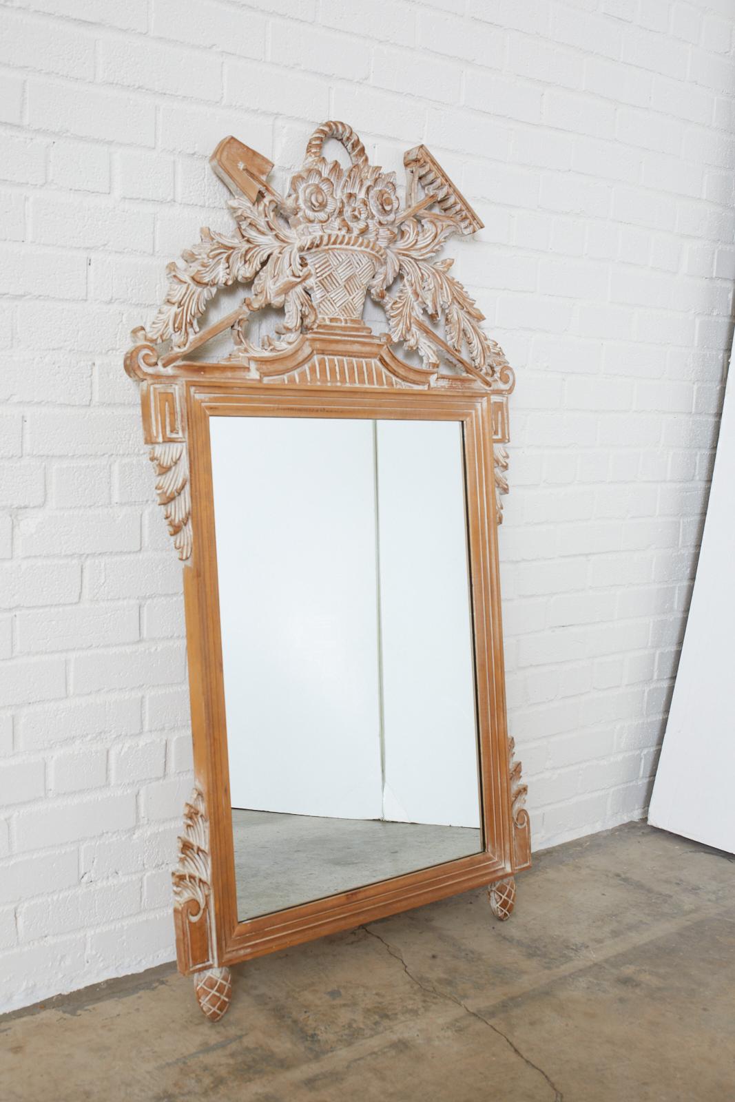 Hand carved oak wall mirror with a garden motif featuring a basket of flowers with cascading acanthus leaves and garden tools made in the Louis XVI style. Sits on pinecone feet with foliate accents on each corner. Has a white washed finish.
 