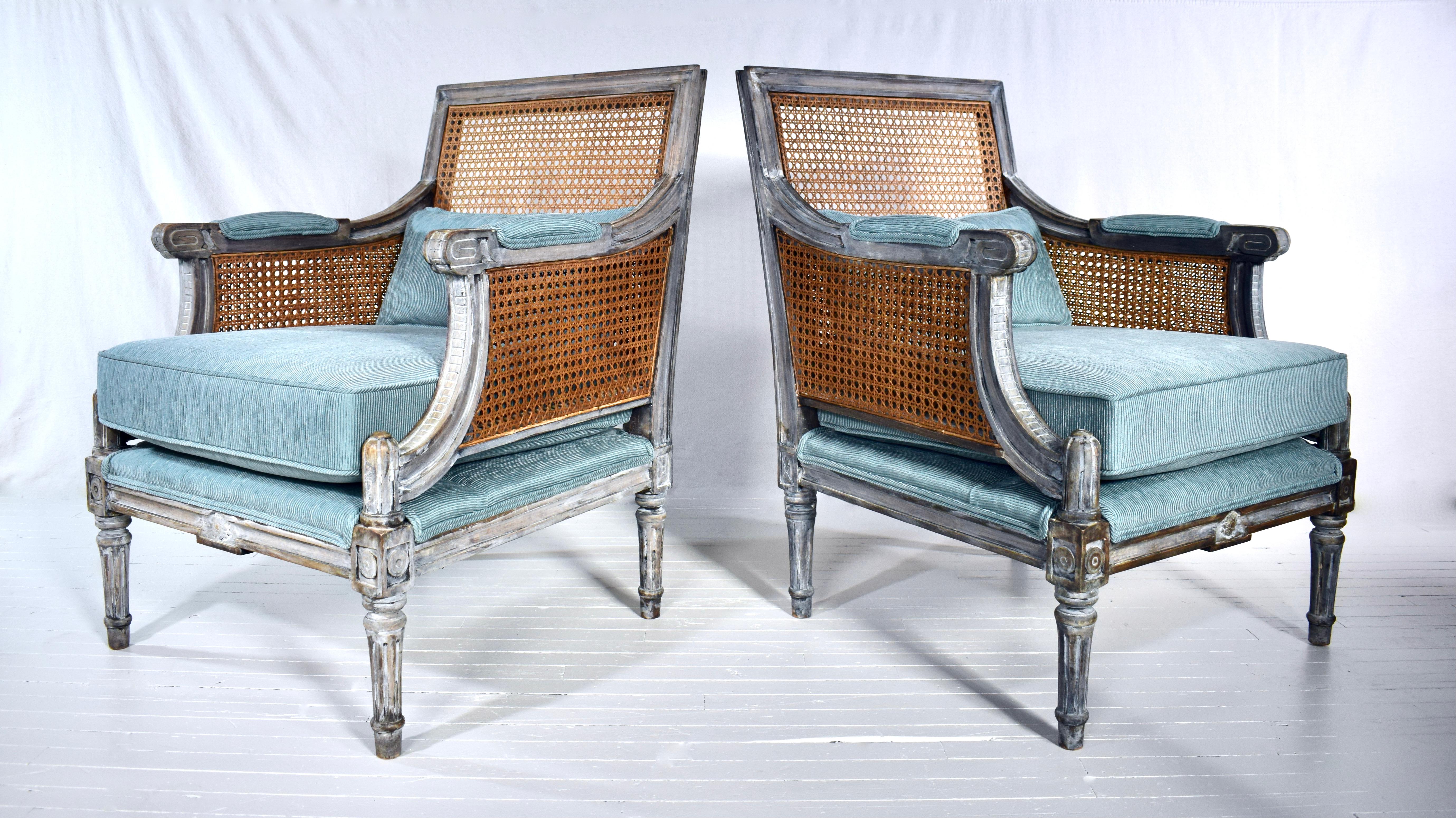 A fully restored pair of French Louis XVI style Bergere Chairs in new French Blue textured upholstery. Exquisite features include double caned arms, caned back, custom bolster cushion & carved frames with intensionally distressed painted finish;