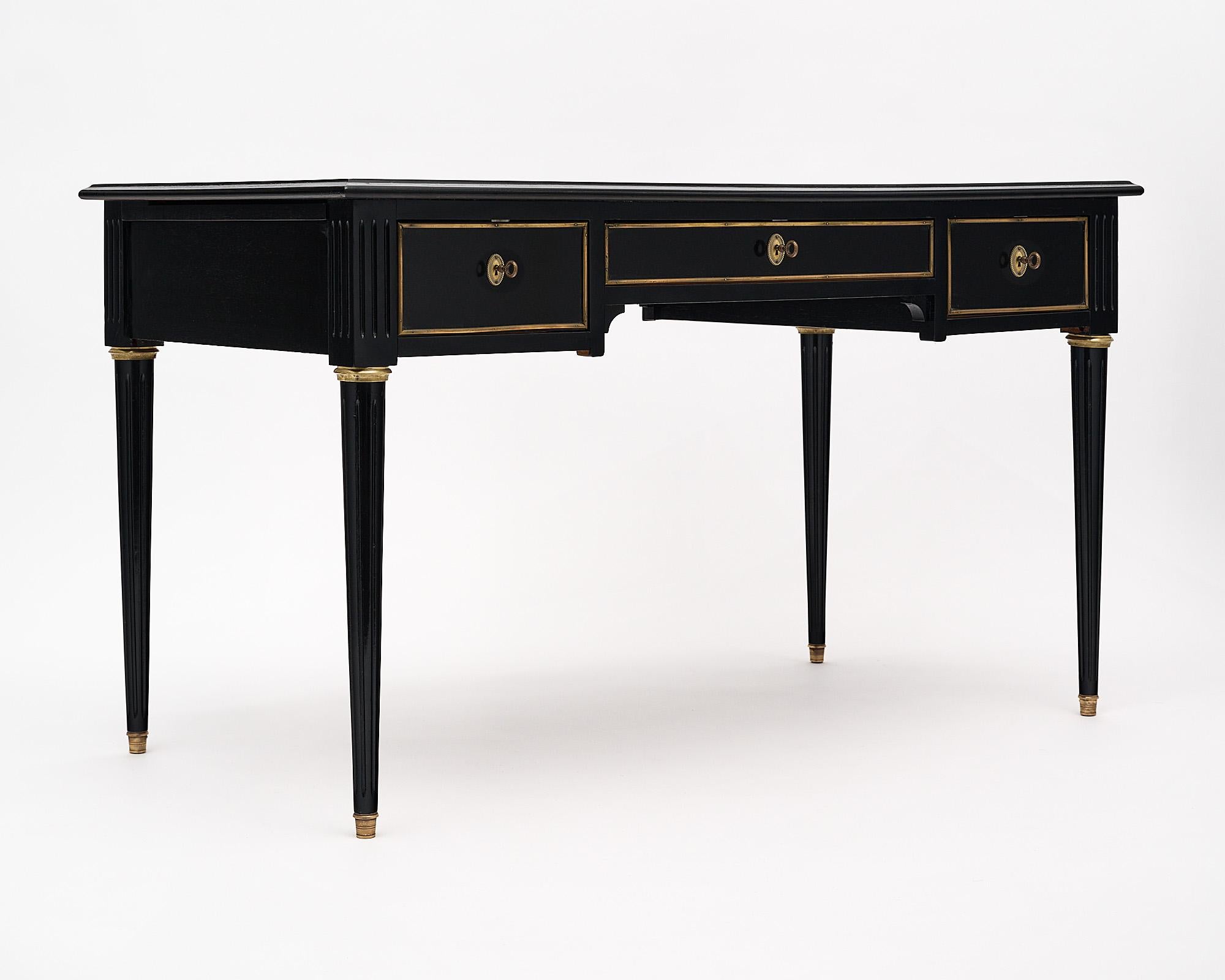 Desk, French, in the Louis XVI stye and made of ebonized mahogany that has been finished in a lustrous museum quality French polish. The French neoclassical desk features three dovetailed drawers and gilt brass trim and hardware throughout. The