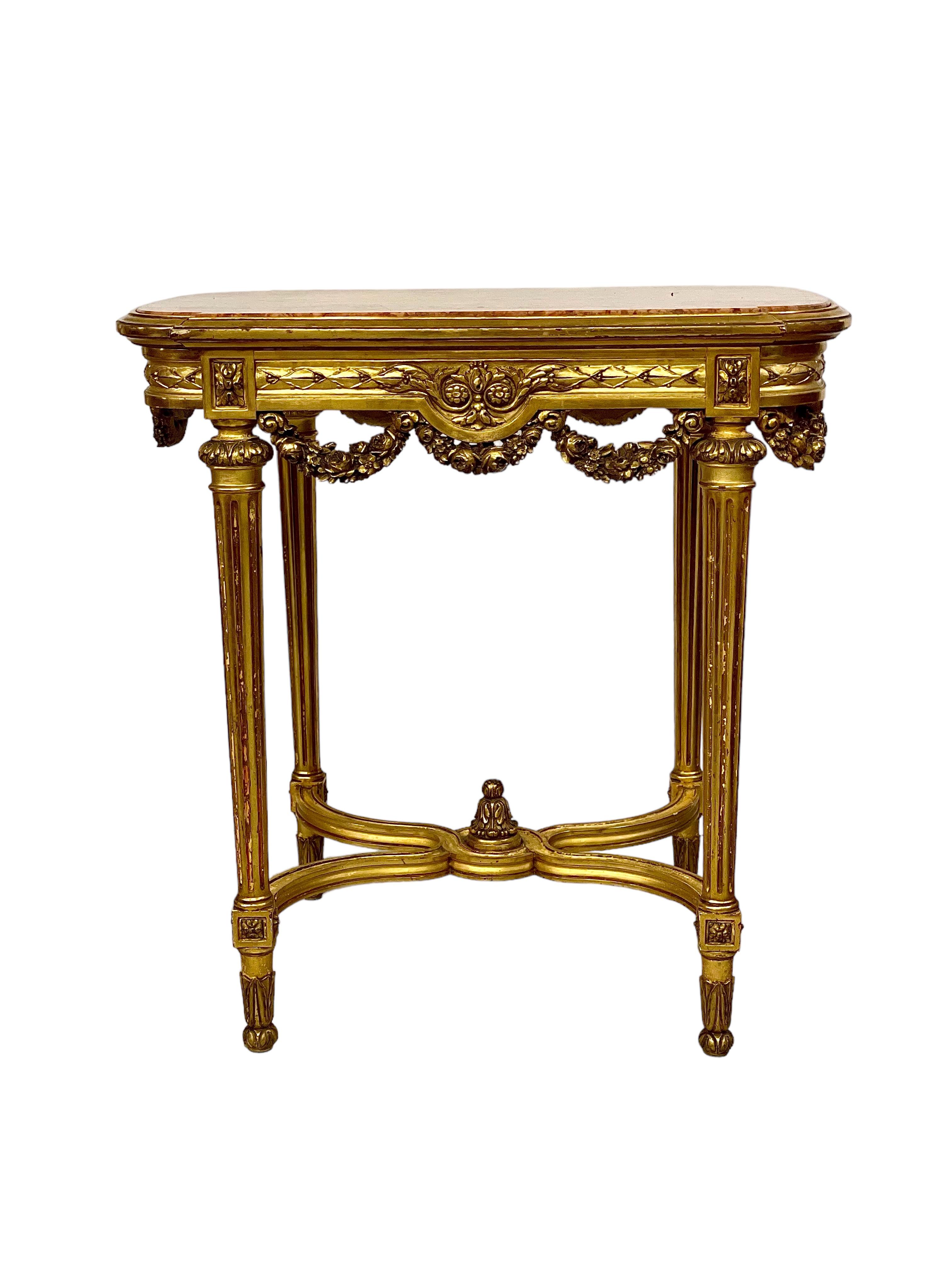 A pretty little Louis XVI style centre table (or 'Table de Milieu') in carved, moulded and gilded wood, and ornately decorated around and below its apron with swags of flowers and carved motifs. A curved X stretcher joins the four fluted and tapered