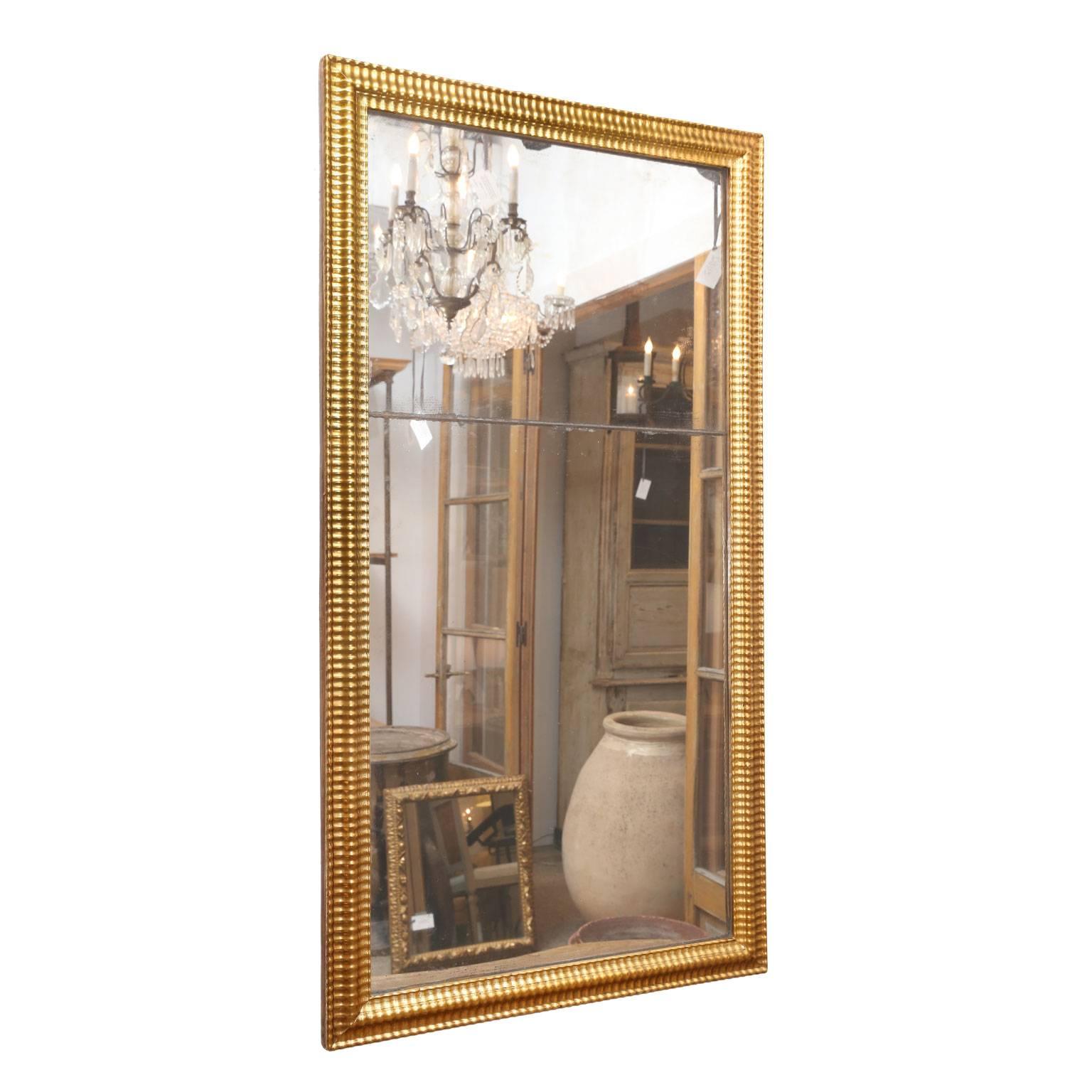 Louis XVI giltwood mirror, two tones of gilding adorn frame surrounding a bipartite mirror plate. Mirror’s reflection is near-pristine with only a few age spots. Subtle amounts of diamond dust cluster around mirror’s edges and joint where the two